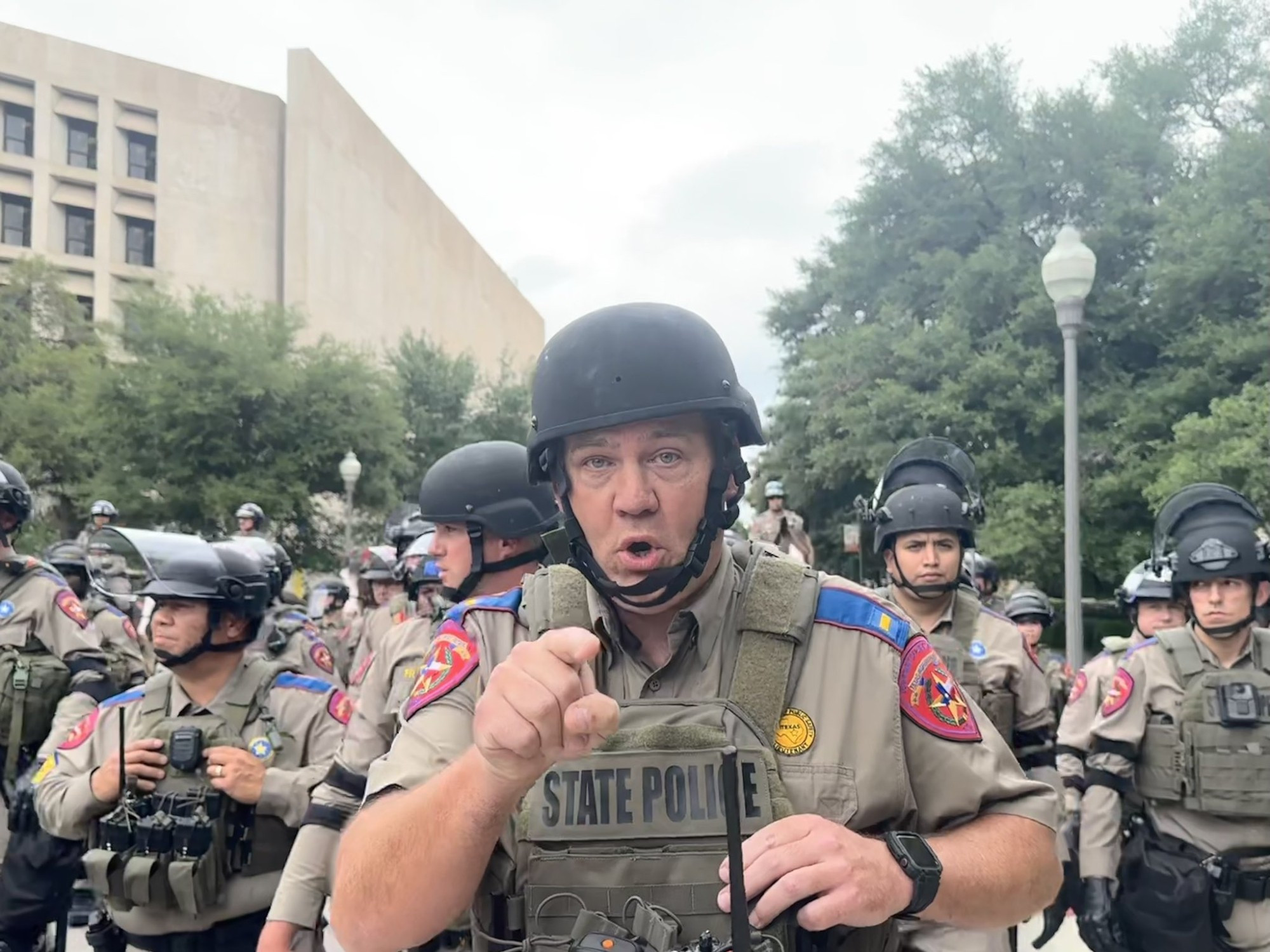 A bunch of Texas DPS State Troopers prepare to invade The University of Texas. There's a cop in the front pointing at the camera. He's trying very hard to look mean, but he really just looks like a dick.