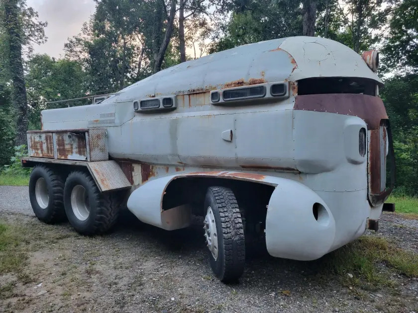 The "Herkimer Battle Jitney" from the movie "Mystery Men". A rounded, bulbous wheeled truck with slit windows, painted grey and dull red, with rust on many of its surfaces.