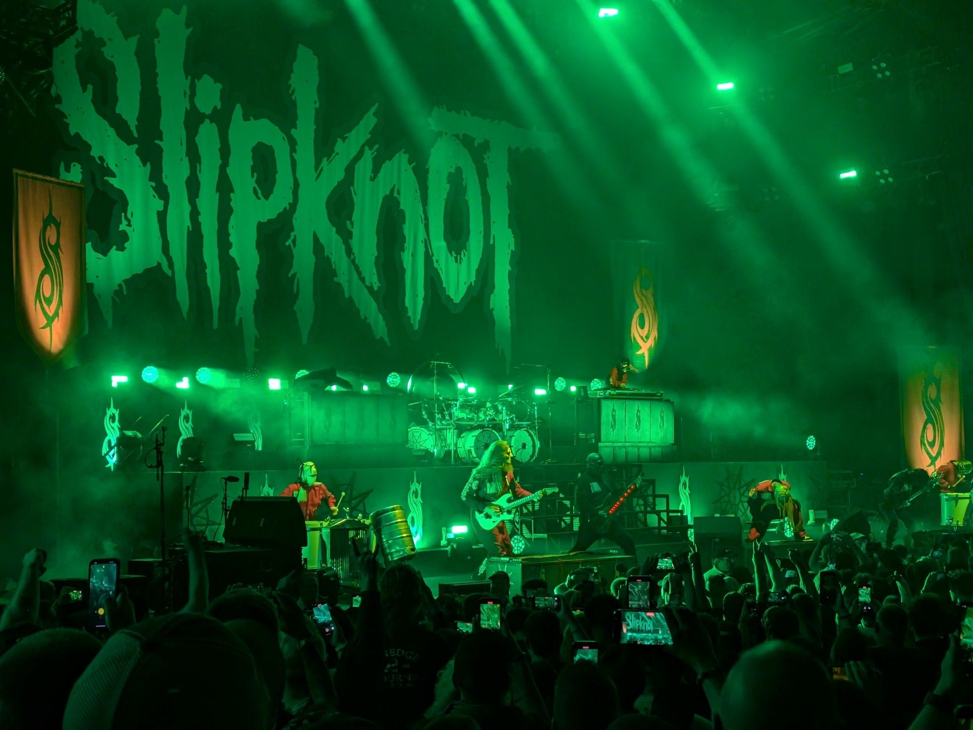 Photo of green hued stage with huge Slipknot banner and band members in red coveralls and make. Hell of a show.