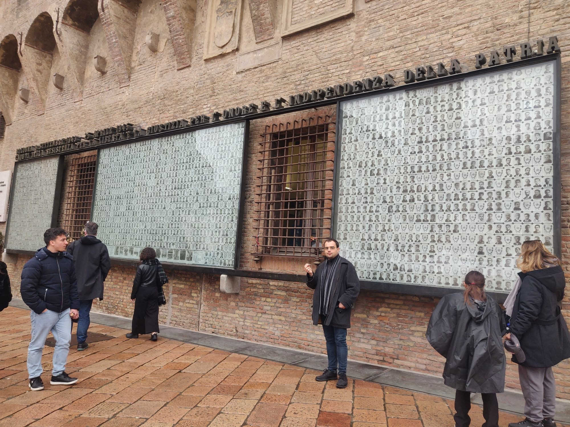 A picture of the memorial to the antifascist fighters of Bologna. It hangs on the side of a seventeenth century brick building and has a black and white photo of each person killed, with their last name and first initial. 
Where a picture wasn't available there's a star and their name.