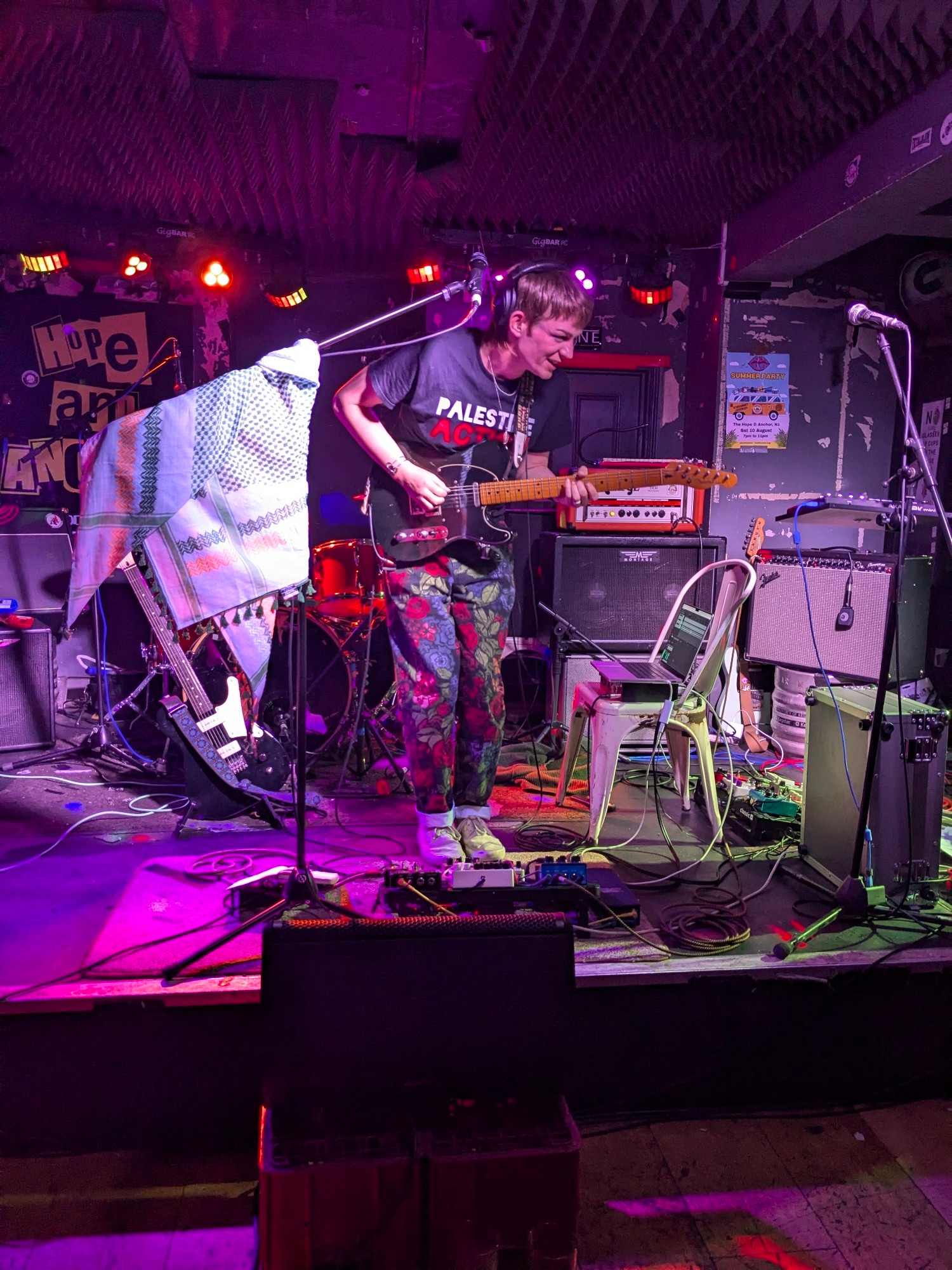 @themenniss.harpy.zone on stage playing guitar and wearing a shirt that says Palestine Action