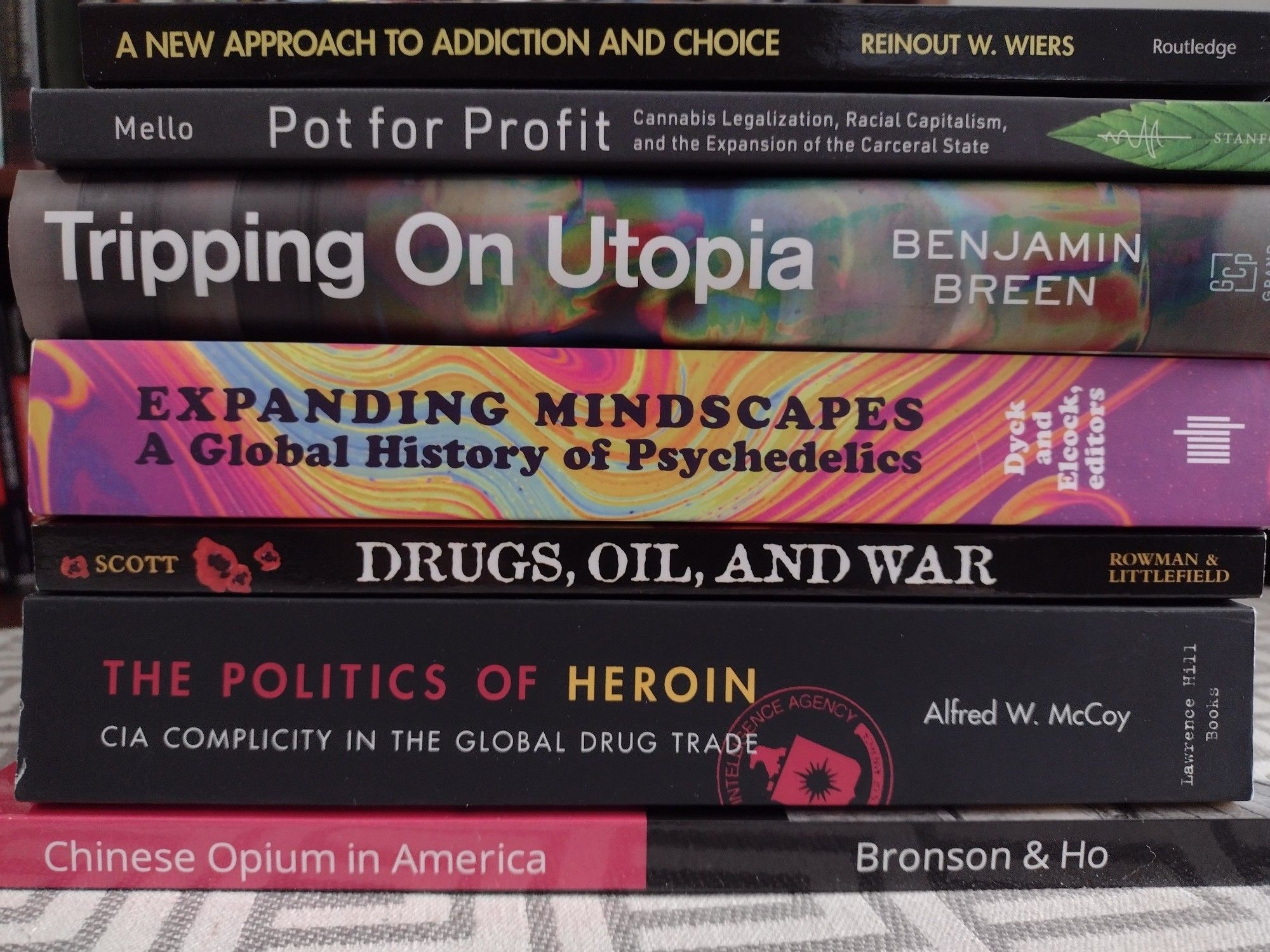 A stack of books titled.
A New Approach to Addiction and Choice by Rein out W. Wipers.
Pot for Profit by Mello
Tripping on Utopia by Benjamin Breen
Expanding Mindscapes: A Global History edited by Dyck and Elcock
Drugs, Oil, and War by Scott
The Politics of Heroin by Alfred McCoy
Chinese Opium in America by Bronson & Ho