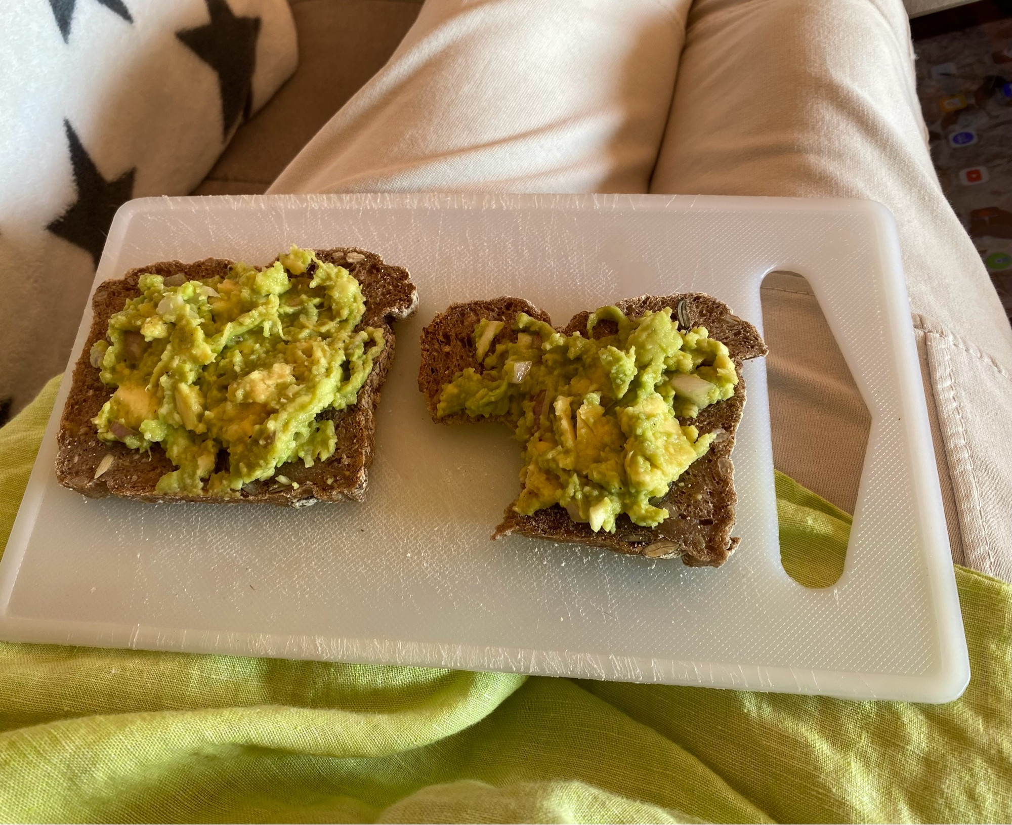 Zwei Scheiben Sauerteigbrot mit Guacamole auf einem Brett auf meinem Schoß, mein Hemd hat die gleiche Farbe wie der Brotaufstrich