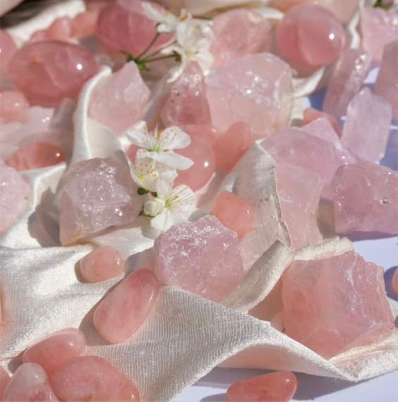 picture of rose quartz on a white fabric and white tiny flowers over the quartz. 