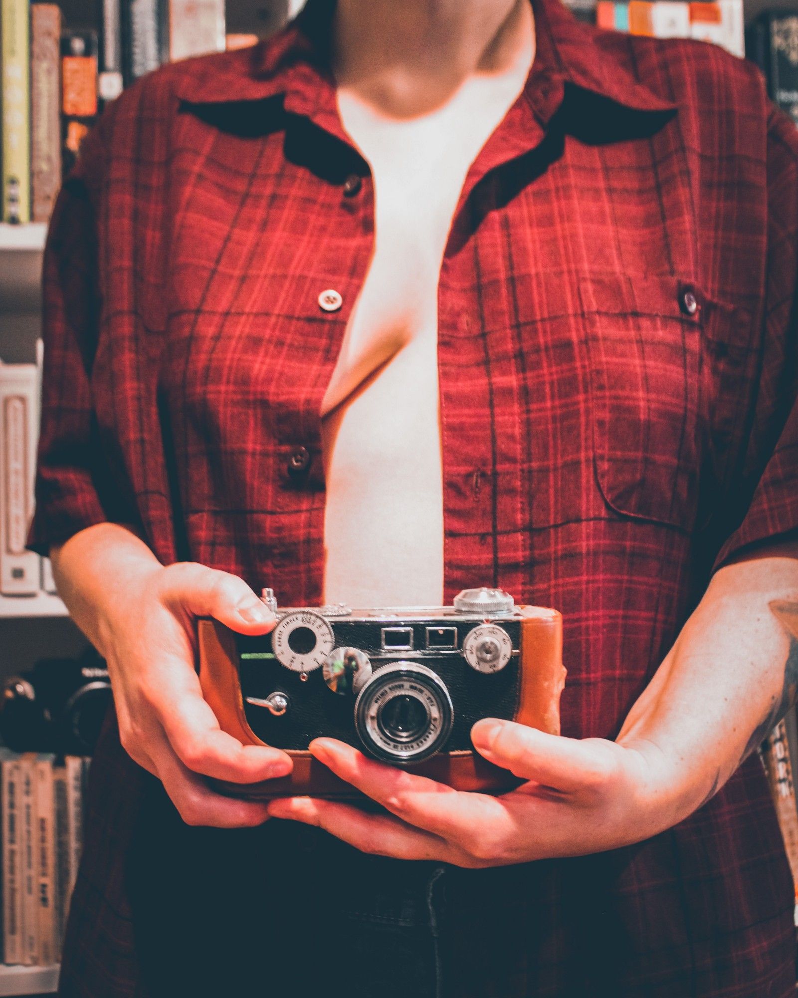 Frankie holding a vintage Argus camera, their shirt open, one breast partly exposed