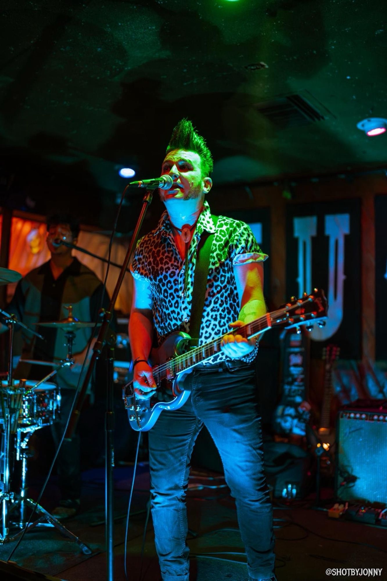 Singer / guitarist Nick Feratu on stage with a blue Gibson SG guitar, shrouded in blue and green light.