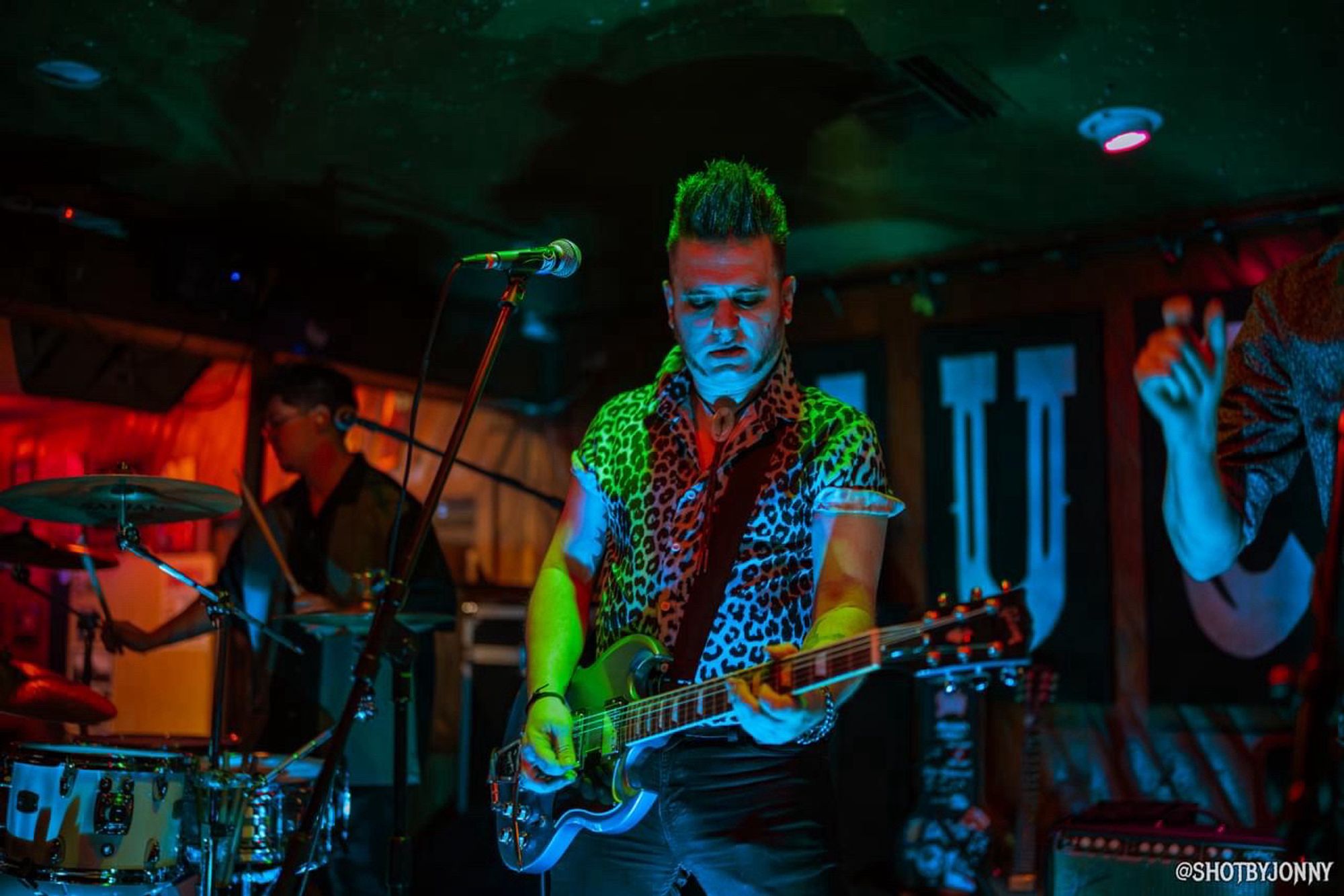 Singer / guitarist Nick Feratu on stage with a blue Gibson SG guitar, shrouded in blue and green light.