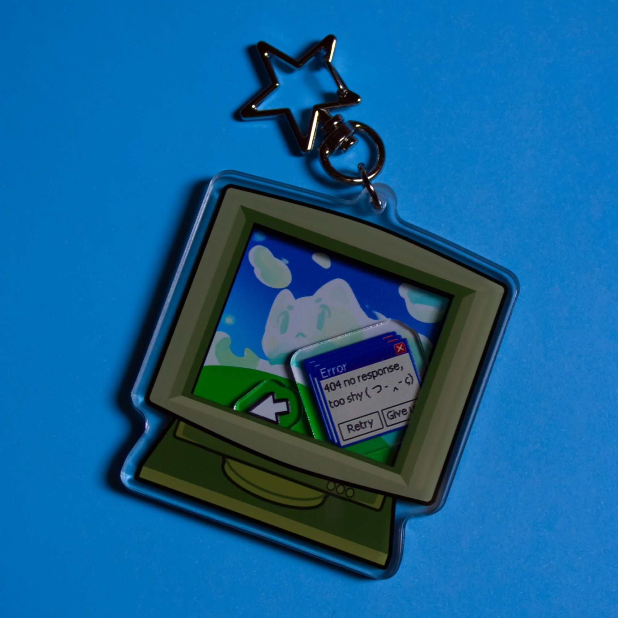 a shaker keychain that looks like an old pc with two little charms inside (one is a cursor and the other one an error popup). The background inside the computer is a cat cloud. The clasp is starshaped.