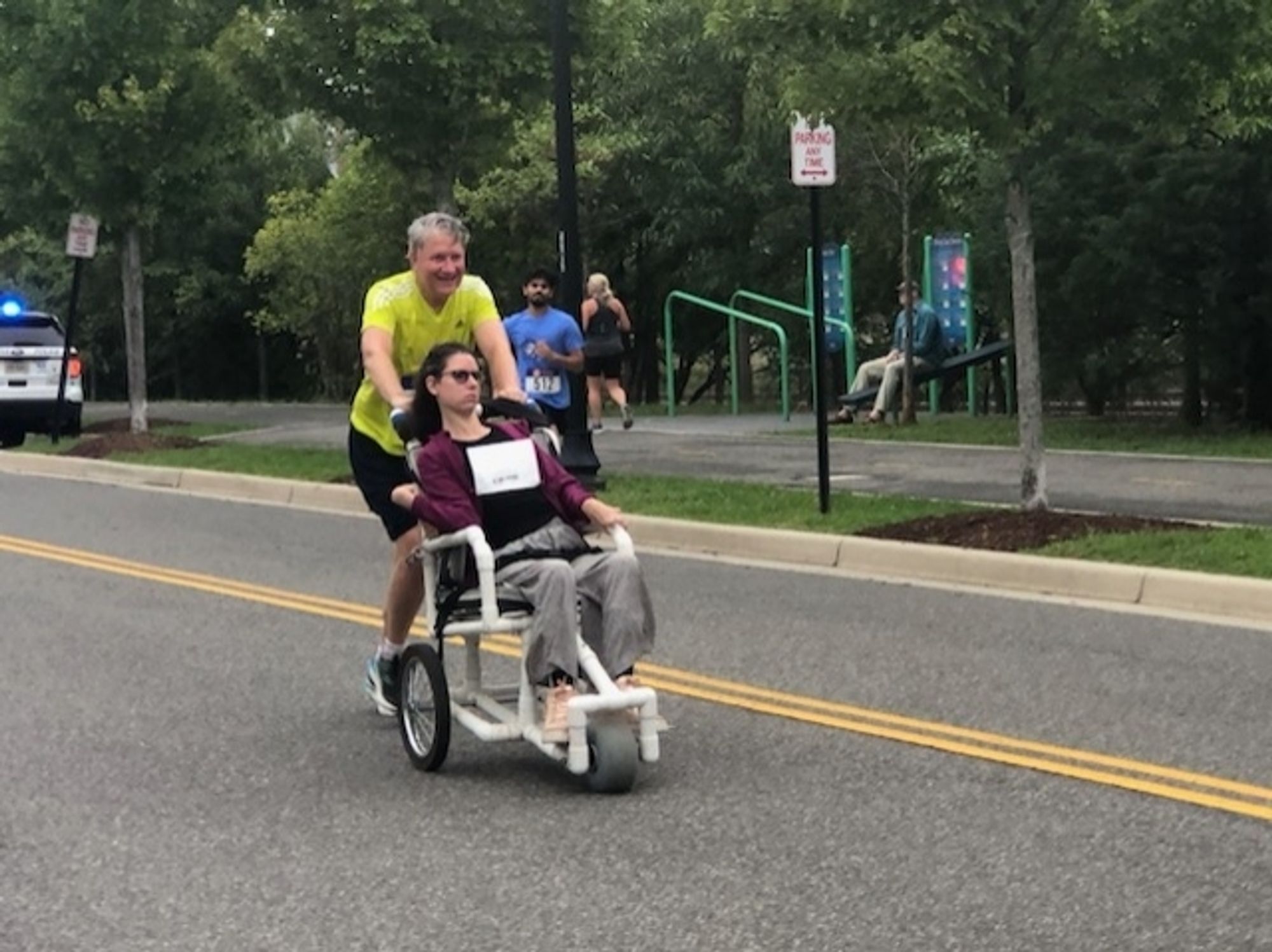 Young woman in a wheelchair finishing a running race. She is pushed by the sweaty heap of barely-functioning man that is her father at that point in time.