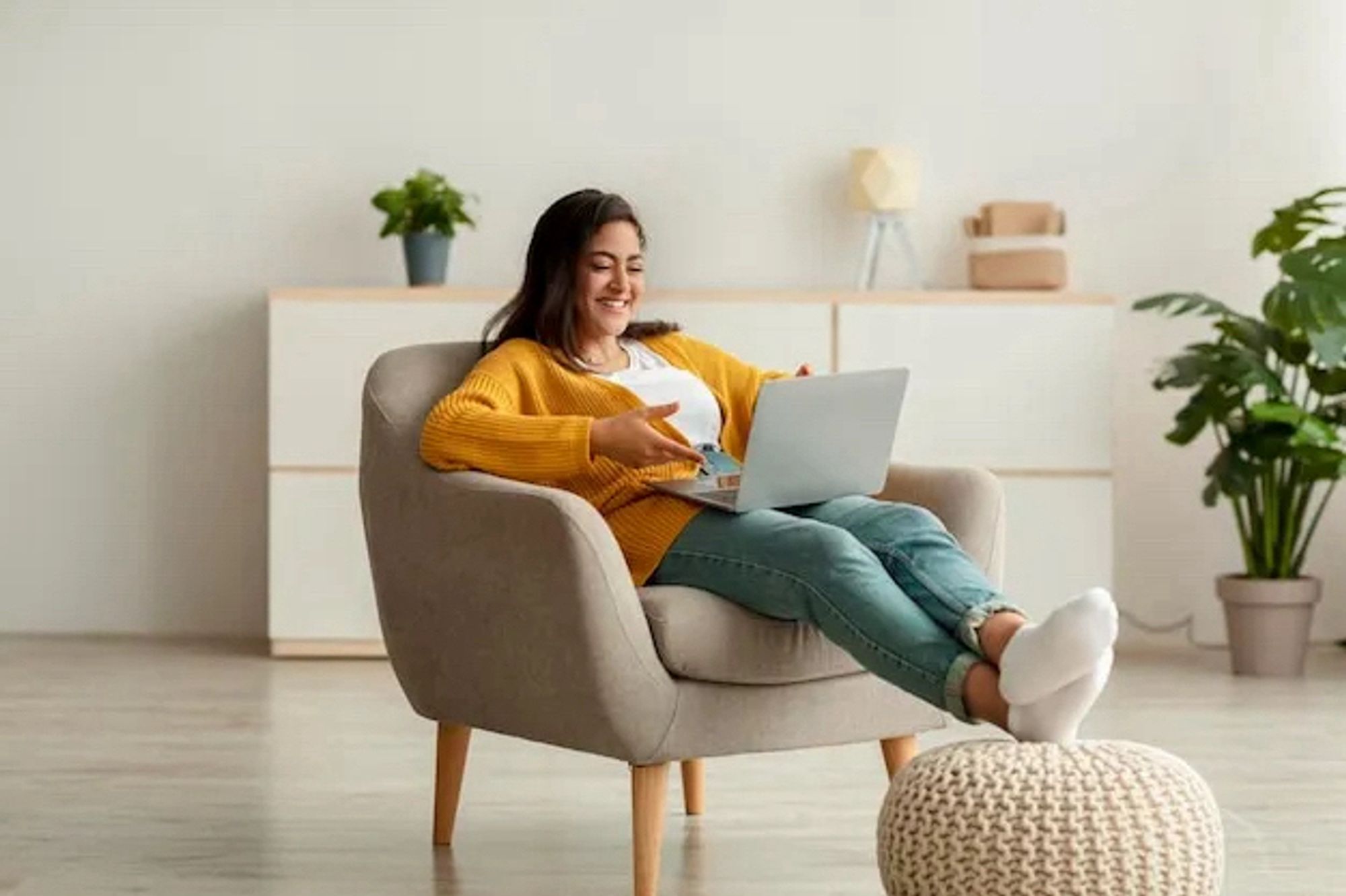 Woman in a chair with her feet up smiling at something on her laptop.