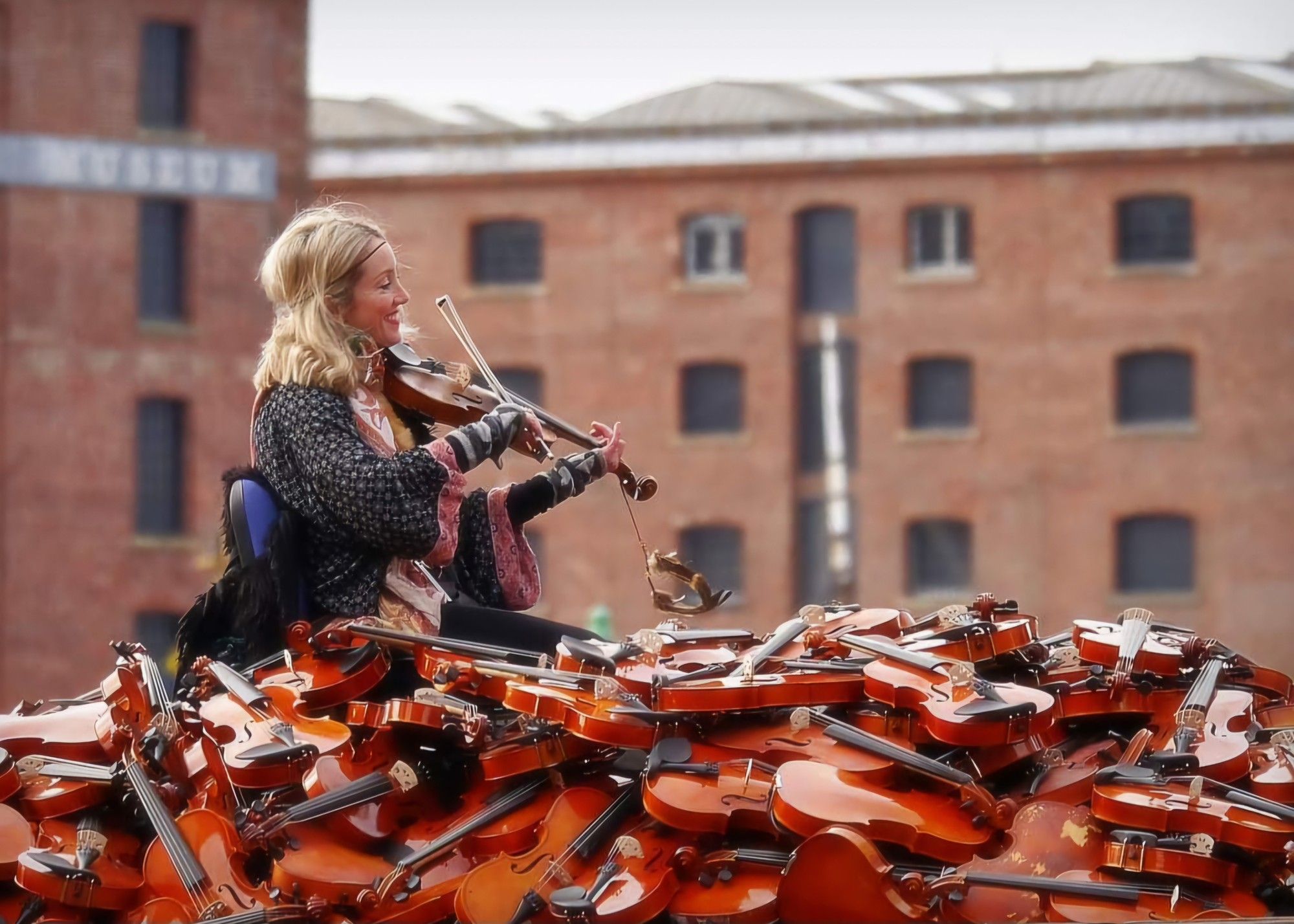 A female violinist plays atop a float full of violins as it progresses alongside Albert Dock, Liverpool. October 2018.