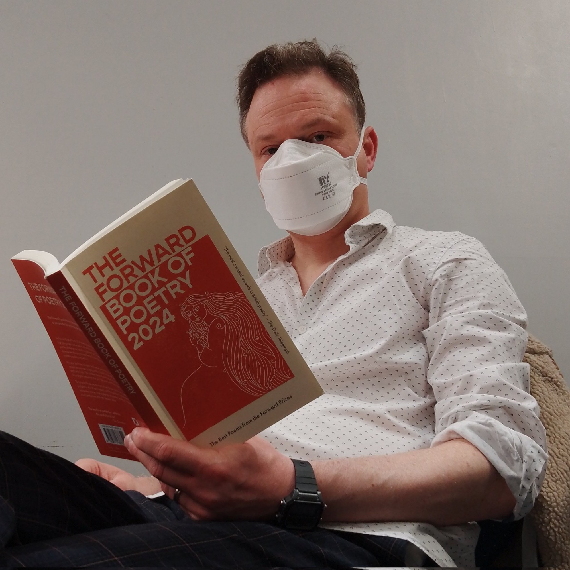 Man reading book of poetry and wearing respirator mask.