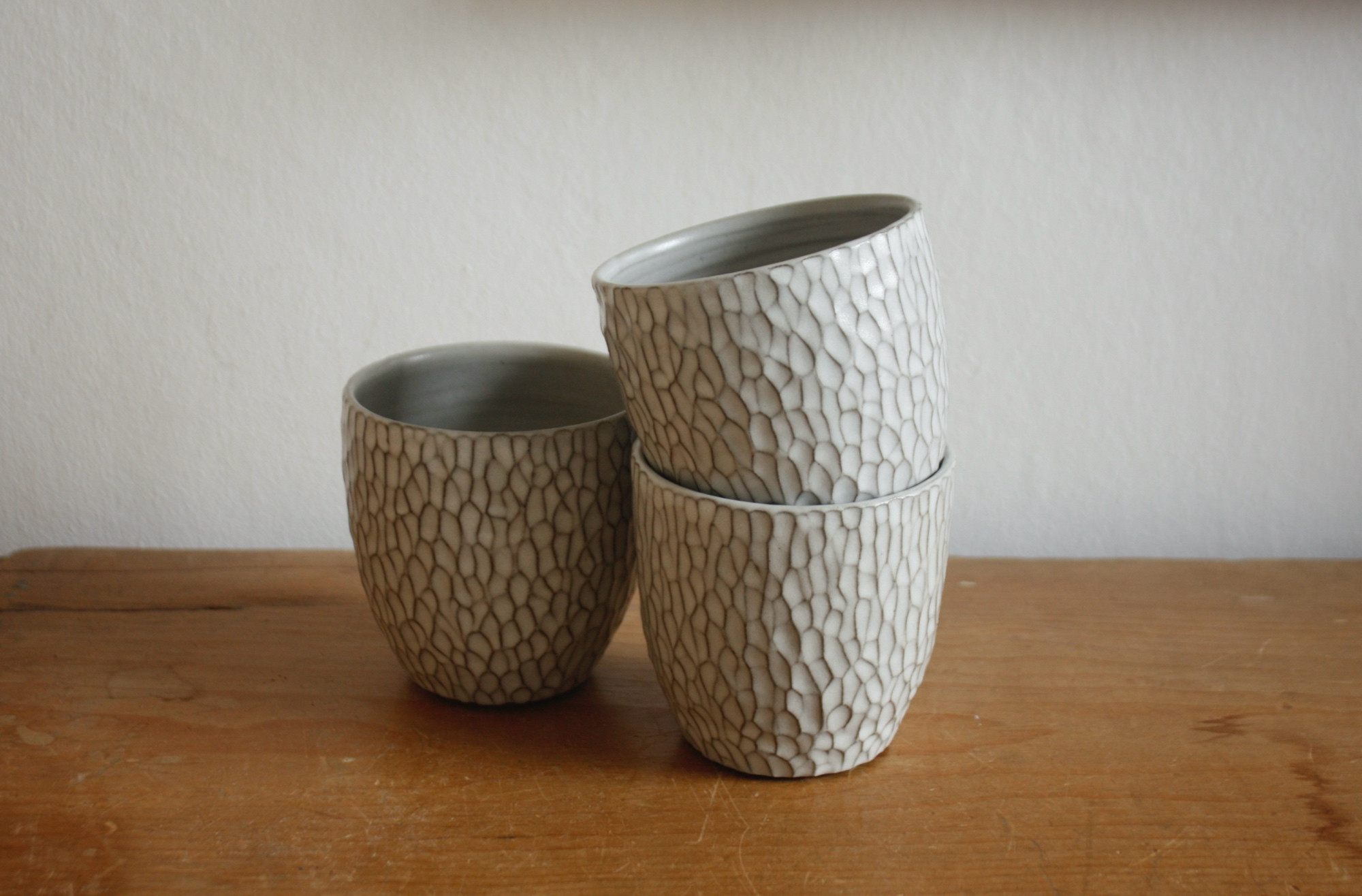 Three carved white beakers on a pine surface against a white background. 
