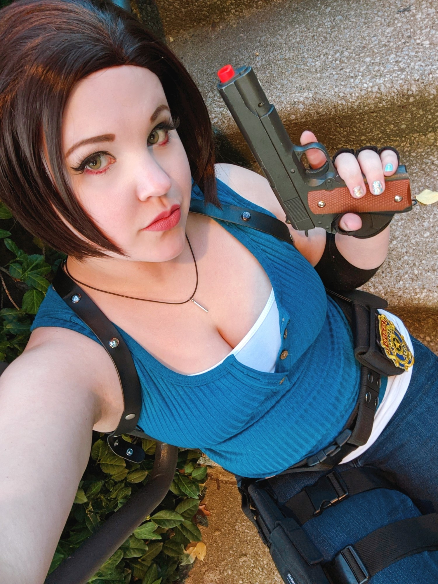 Linds sits on a flight of stairs, dressed as RE3 Remake Jill Valentine. She holds a pistol and stares at the camera intensely.