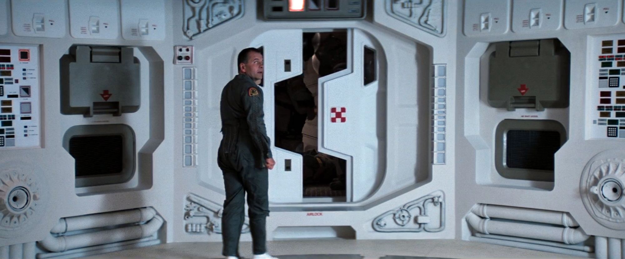 still from Alien (1979): Ash stands, looking back over his shoulder as the airlock door in front of him opens