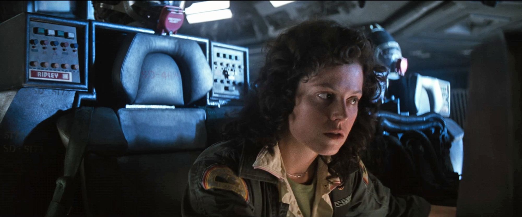 still from Alien (1979): Ellen Ripley sits on the bridge of the spaceship Nostromo, leaning forward as she talks over the radio with Dallas