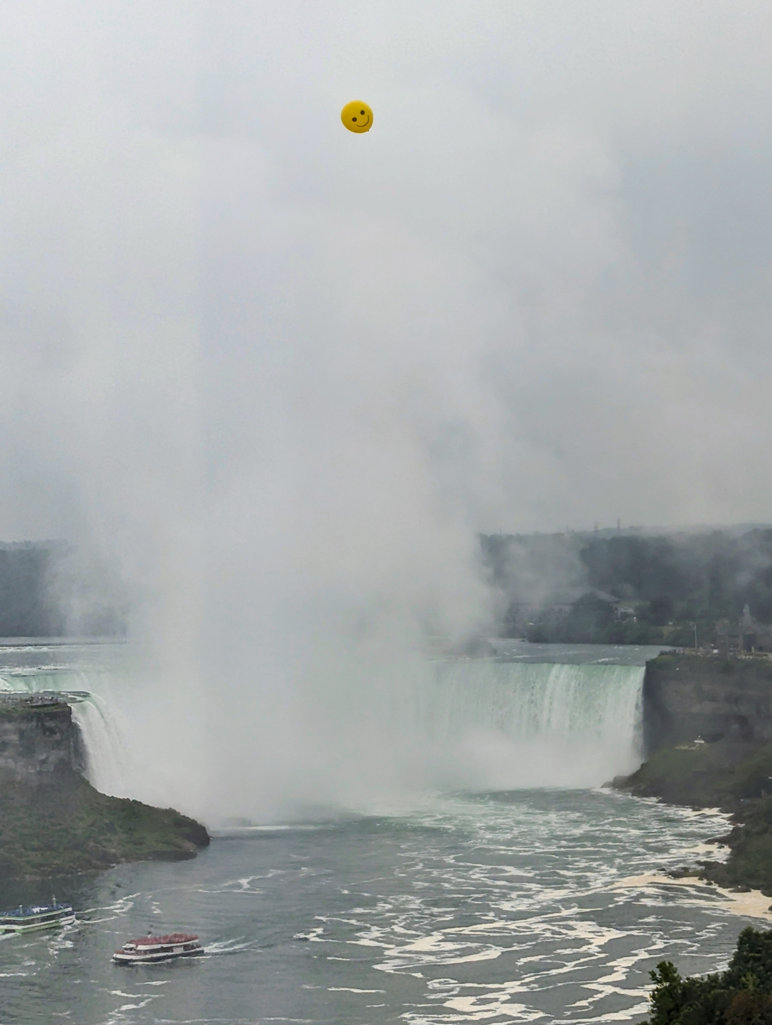 Yellow smiley balloon floating above misty Niagara Falls.