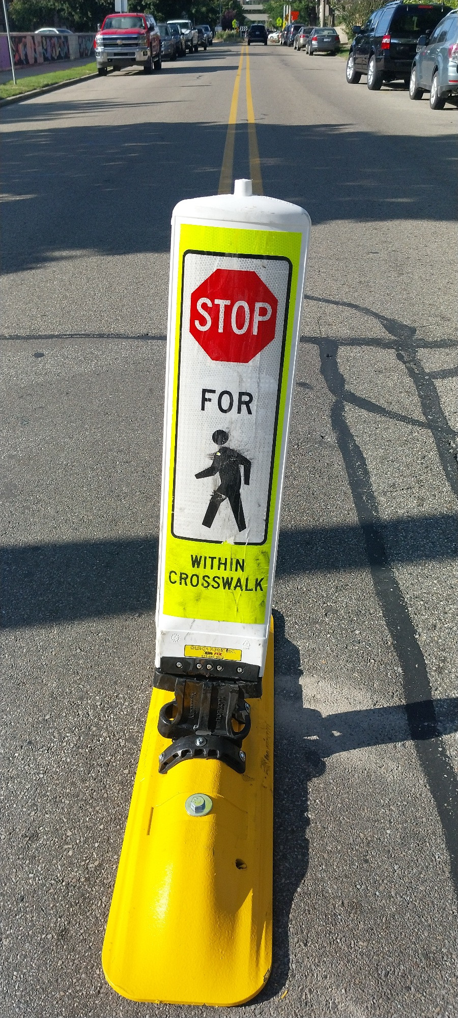 A "stop for pedestrians" mid-road sign. It shows clear signs of having been struck already.