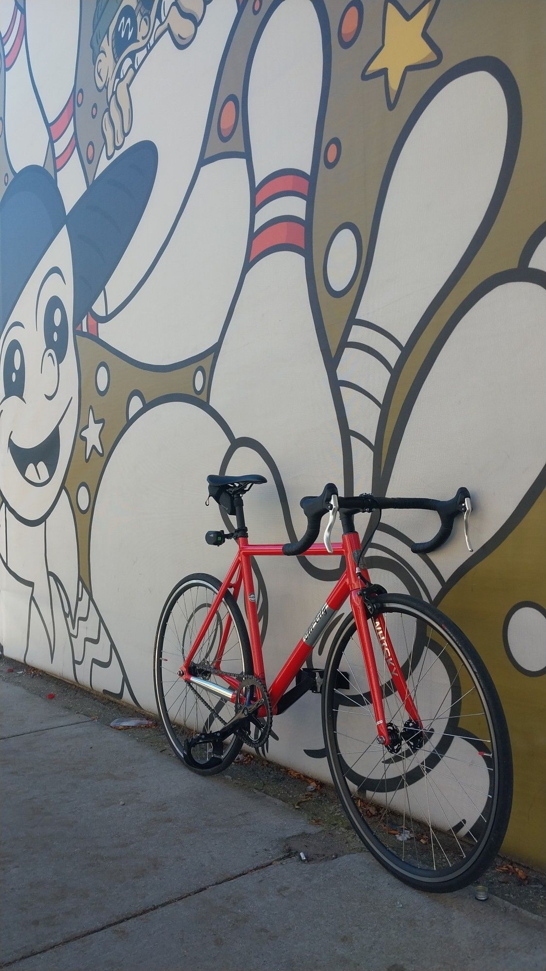 Pink All City Thunderdome Bicycle in front of a mural featuring some bowling pins and a couple people in the "rubberhose / cuphead" style.