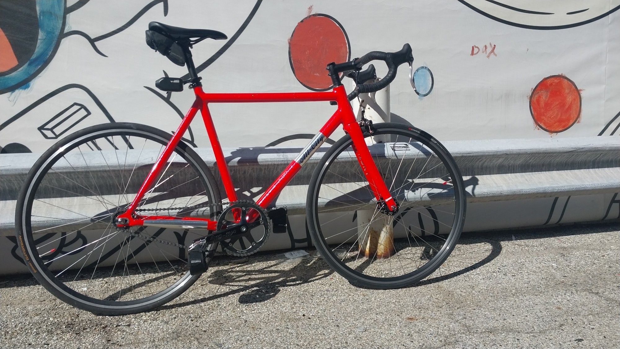 Pink All City Thunderdome Bicycle in front of a mural featuring multiple figures in the "rubberhose / cuphead" style. Close shot on bike.