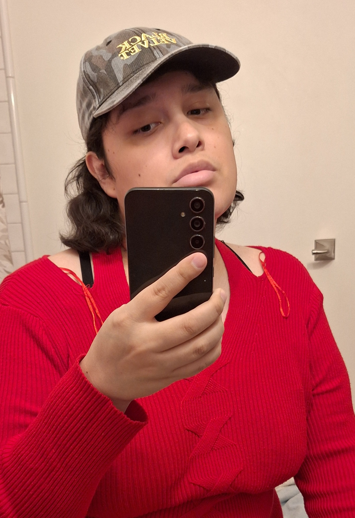 A selfie of myself wearing a red shirt, my favorite military camo hat and doing a slightly pouty expression.