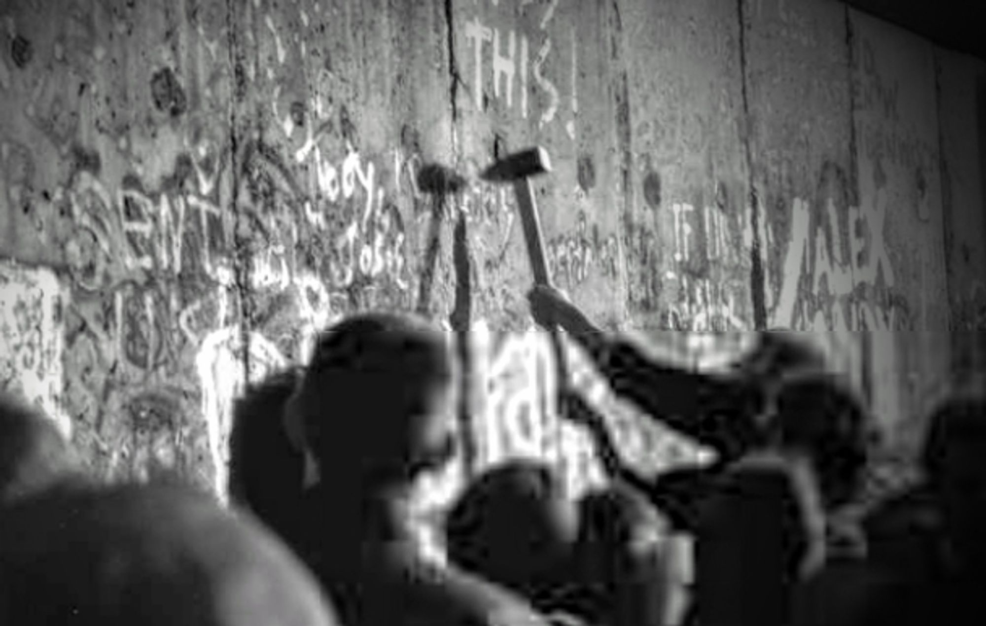 Mensch schlägt mit einem Hammer gegen die Berliner Mauer.