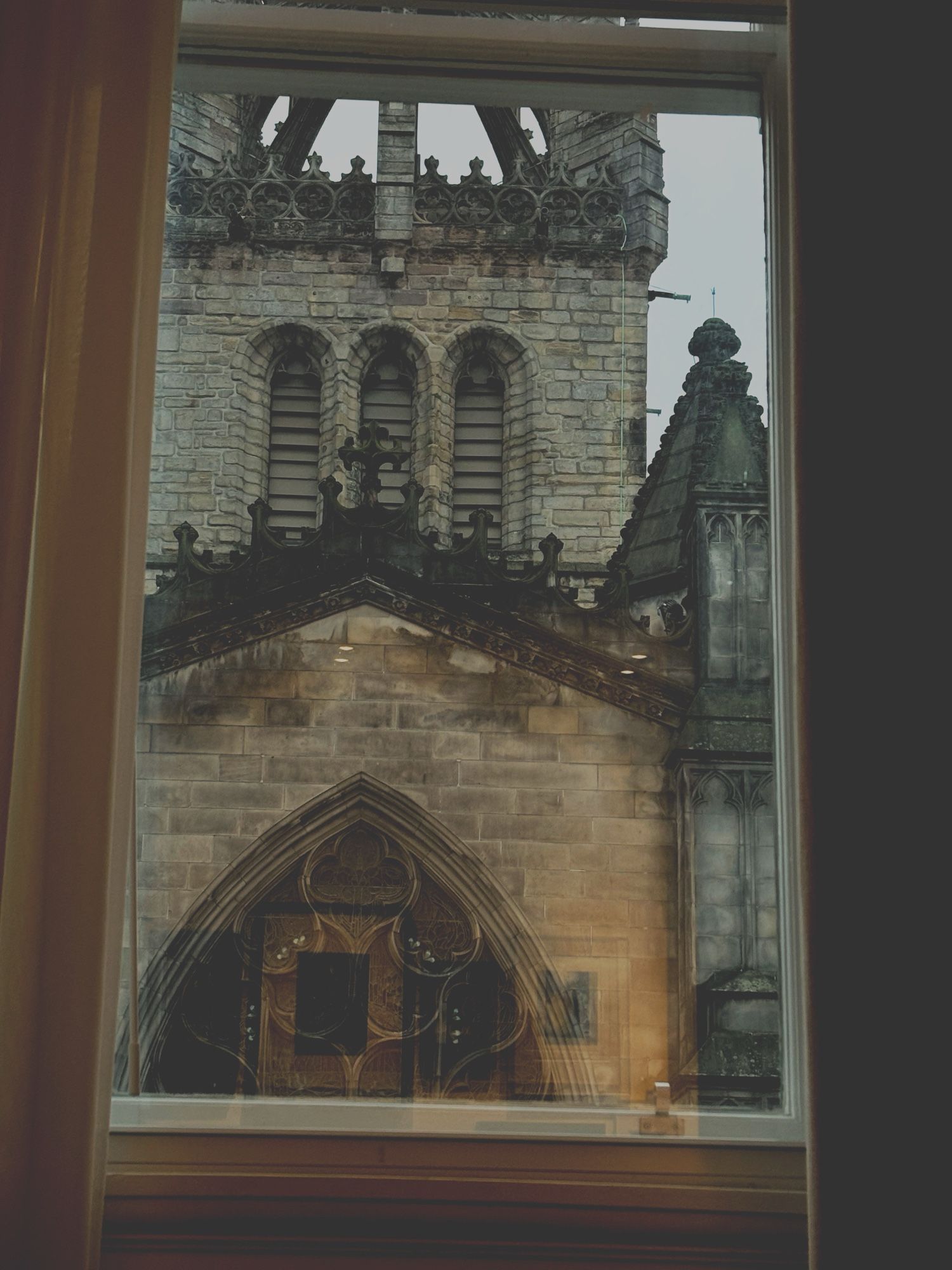 A large cathedral seen opposite the way through a large tall hotel window with the framed pictures hung inside reflecting on the pane.