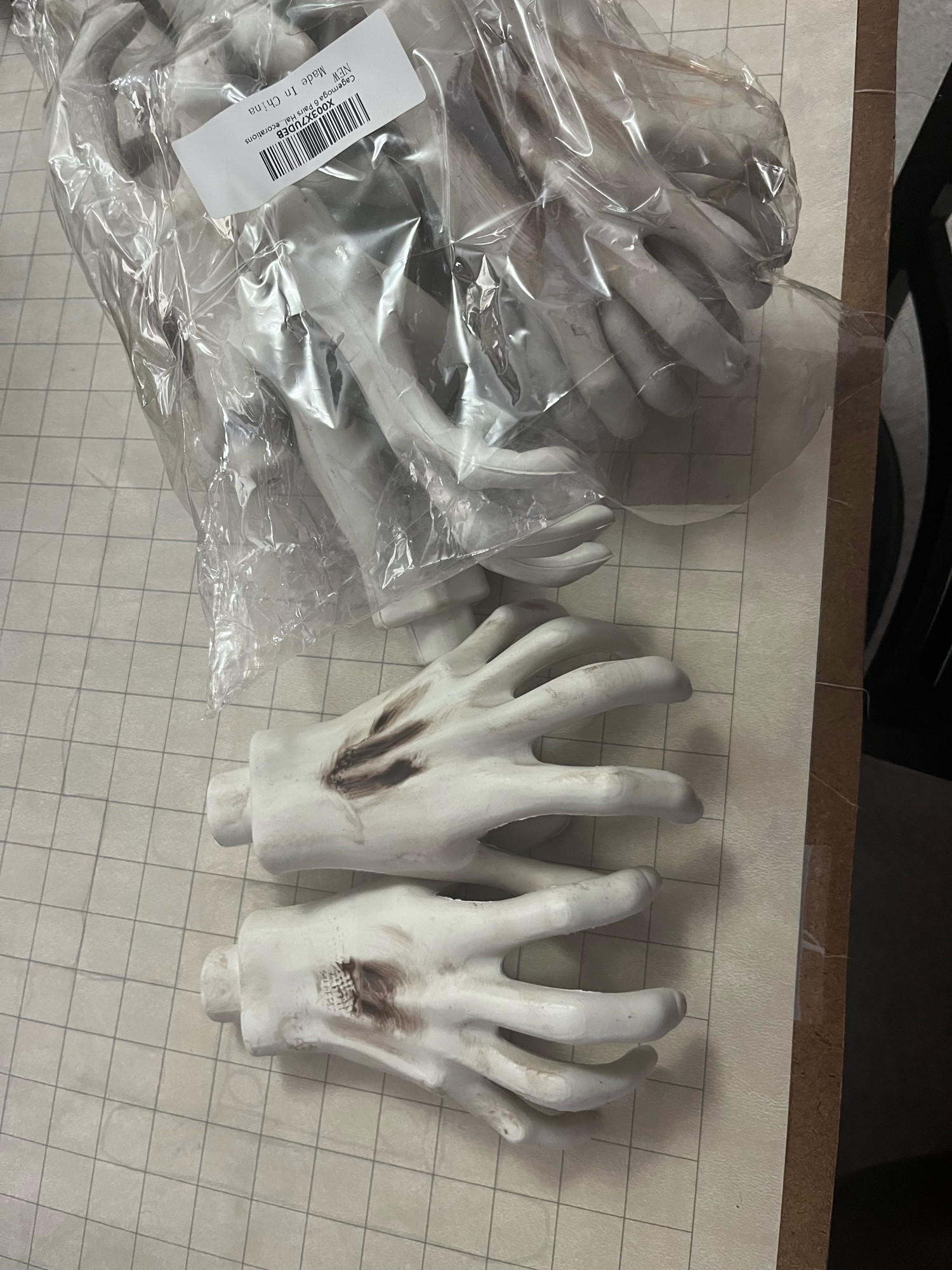 A pair of plastic skeletal hands in a grasping pose next to a clear plastic bag containing five more sets of the same hands.