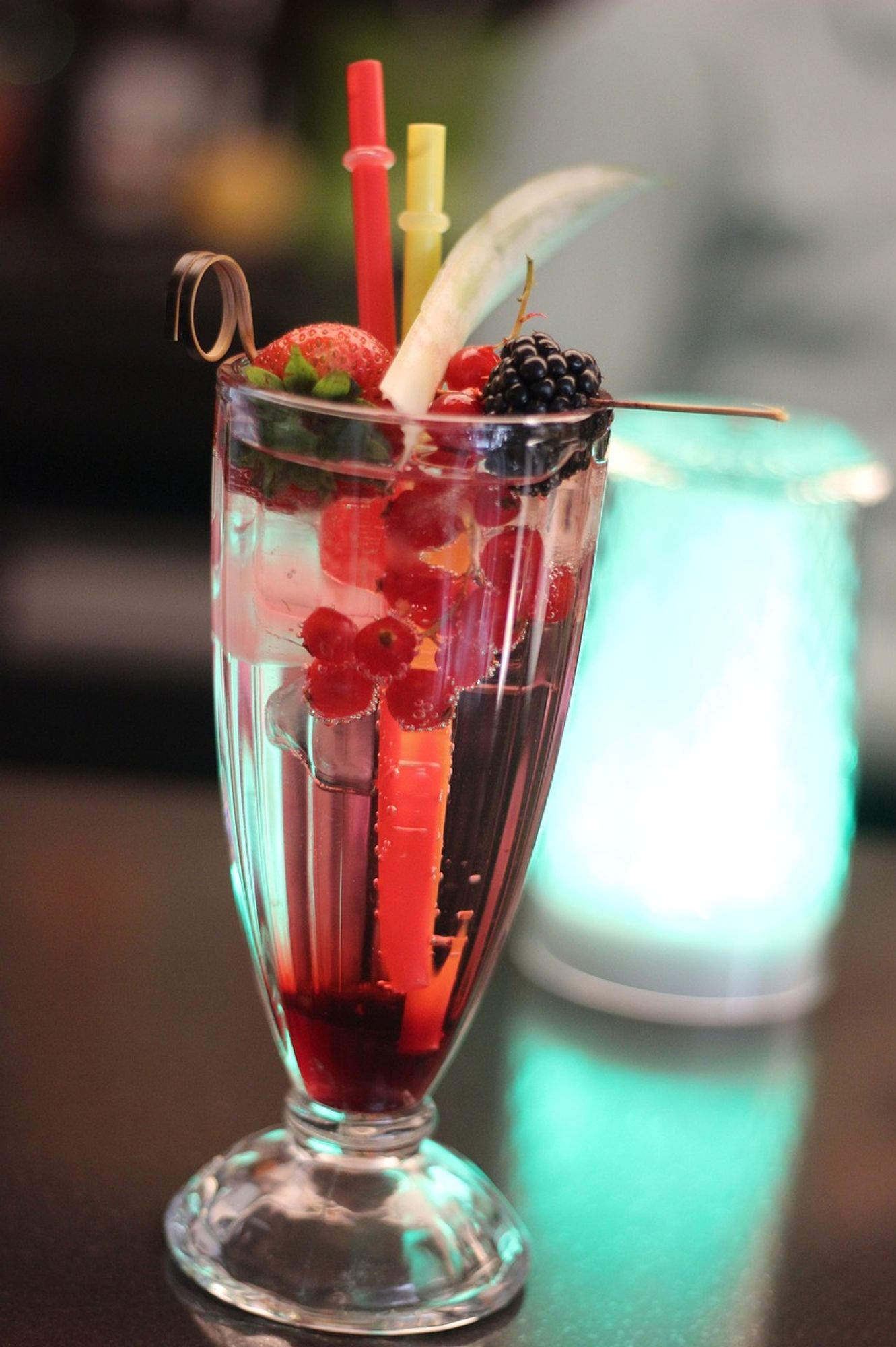 A Shirley Temple cocktail with berries in a tall glass with a small straw.