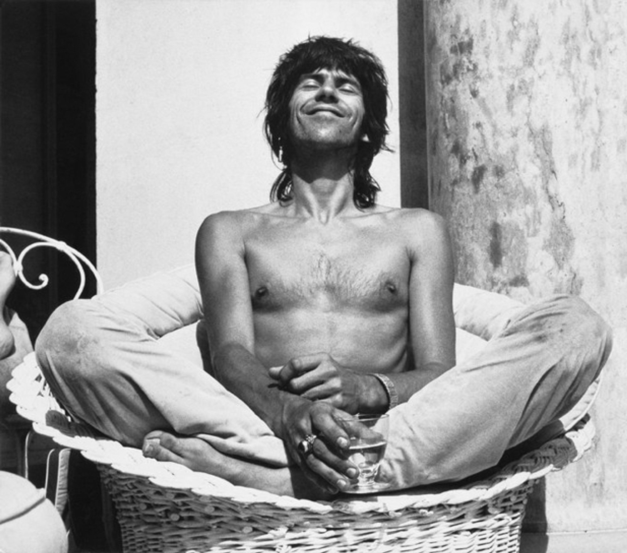 Keith Richards en tailleur torse nu sur un fauteuil en osier