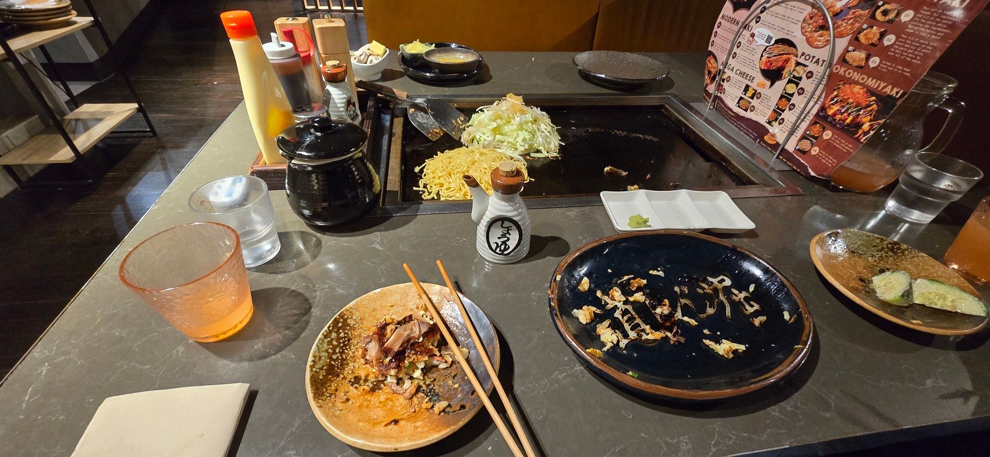 Some plates and things at a teppanyaki restaurant; piles of cabbage and noodles are on the grill