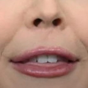 Extreme close-up of a karoline leavitt’s mouth mid-speech. The lips appear heavily lined with lipstick, but have an unusually tight, exaggerated shape—almost like a ventriloquist dummy or AI-generated face. Only the upper teeth are visible.