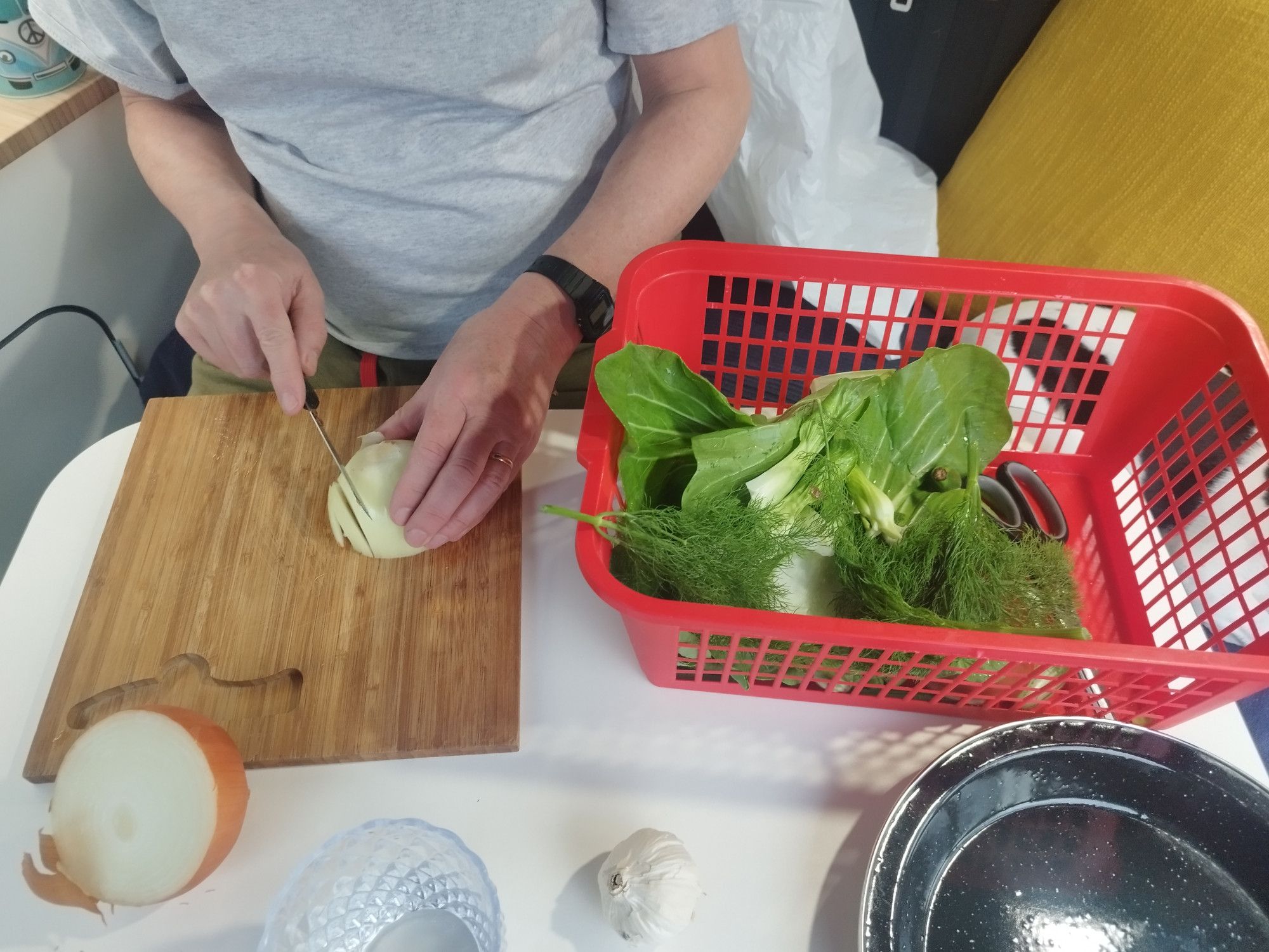 A closeup of a man preparing vegetables. Beside him is a red basket containing Pak choi, fennel, baby aubergines and assorted other goodies.