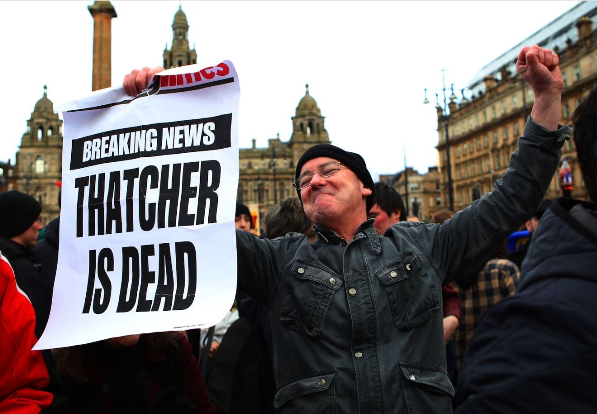 An English man celebrates holding a sign that says "Breaking News: Thatcher Is Dead".