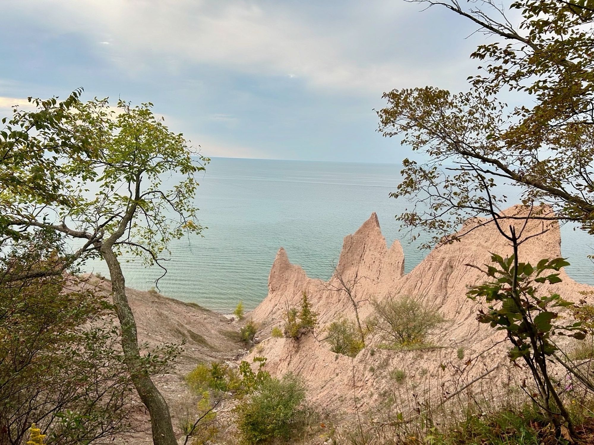 Massive sand and clay bluffs through the trees. Lake Ontario below sky in the background.