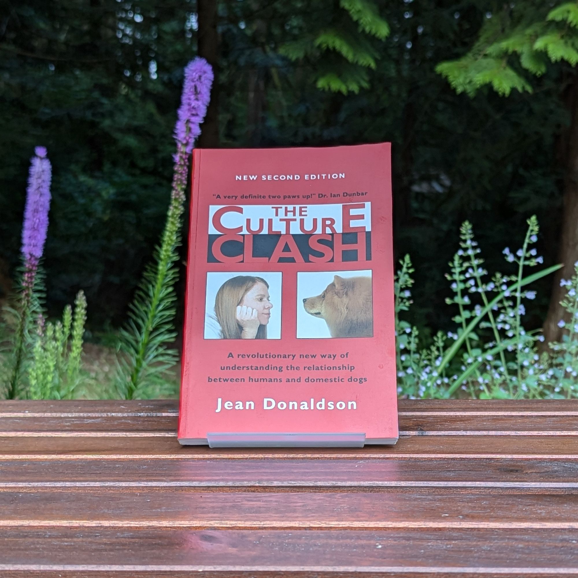 A copy of the book The Culture Clash by Jean Donaldson on a table outdoors with flowers and trees behind.