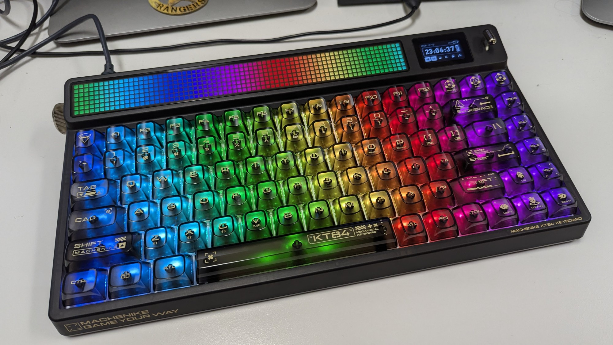 A black keyboard with transparent keys and RGB lights shining through them from below. On the top edge of the keyboard there are 2 screens. A large LED matrix display, and a smaller TFT display.