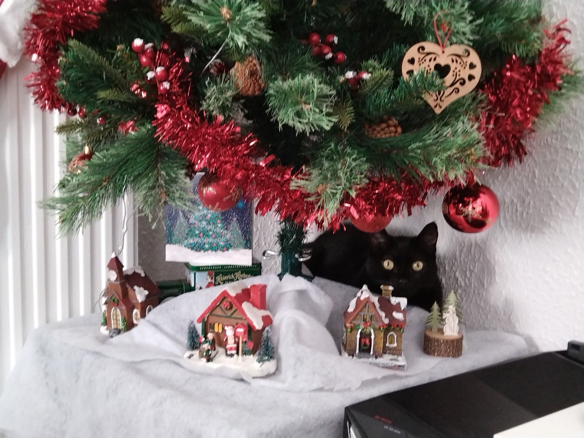 Black cat hidden behind Christmas ornaments under the Christmas tree.