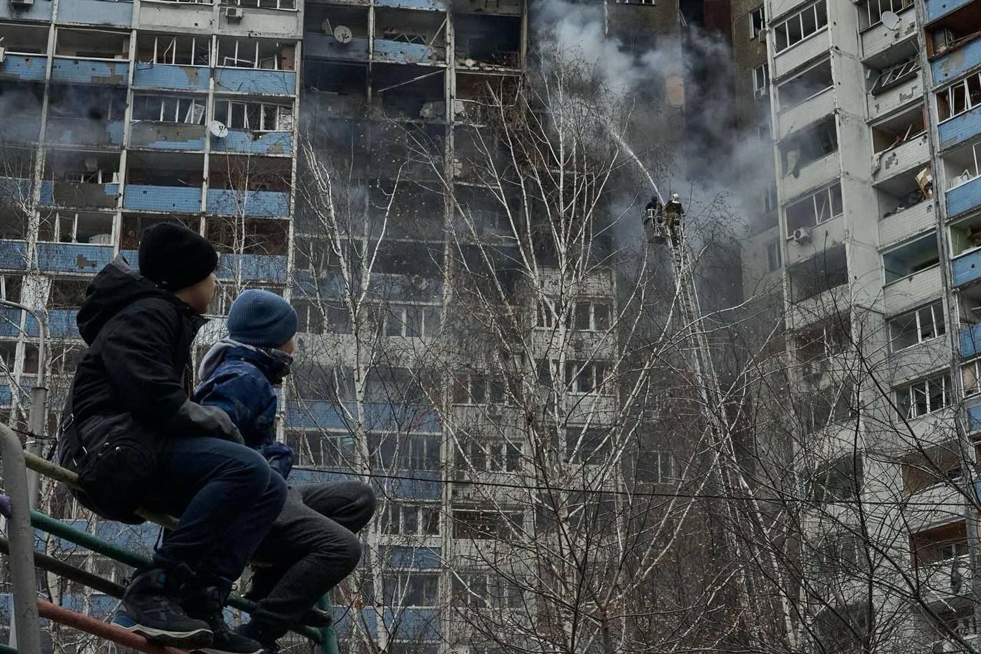 Deux jeunes ukrainiens emmitouflés et assis sur une barrière regarde la barre d’immeuble en flammes bombardée à Kyiv hier matin.
Source inconnue