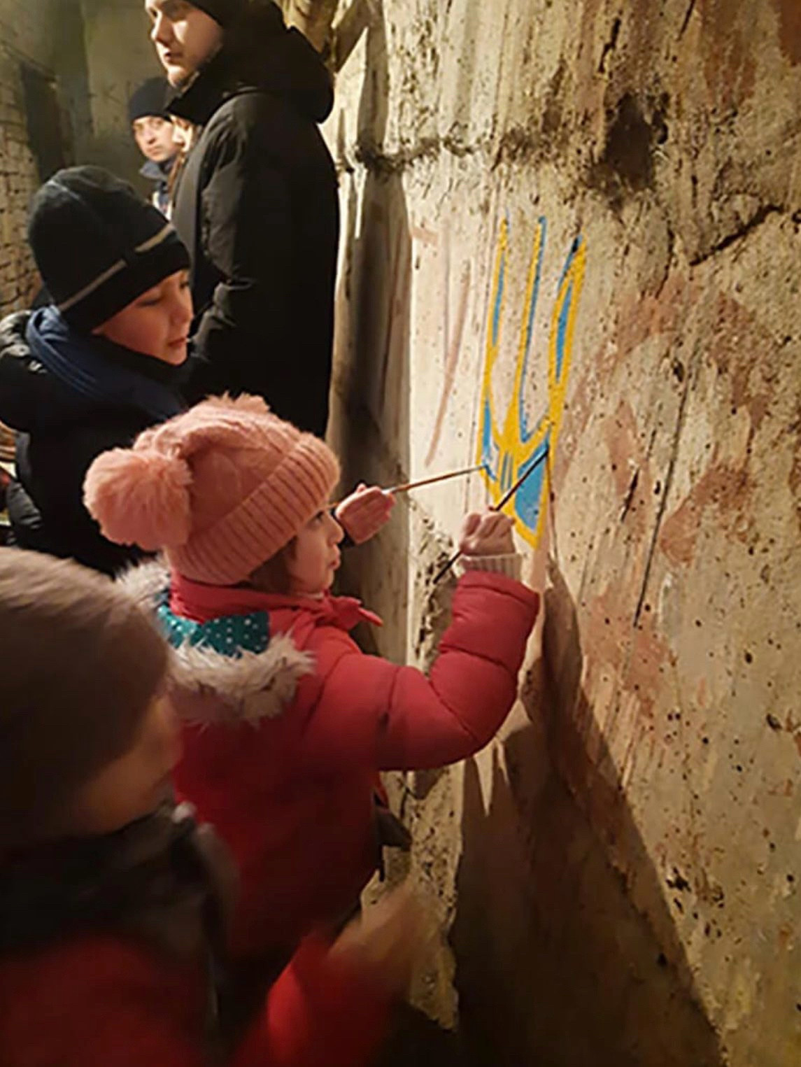 Enfants peignant un mur dans un abri avec les couleurs nationales ukrainiennes