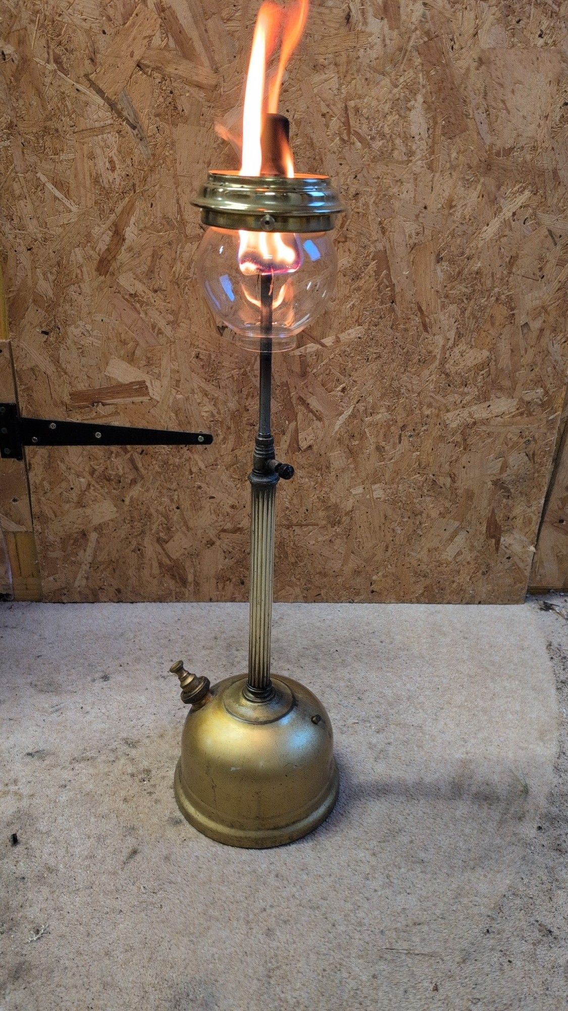 An old Tilley table lamp, in the process of being fettled back to use. It's burning with an orange flame.