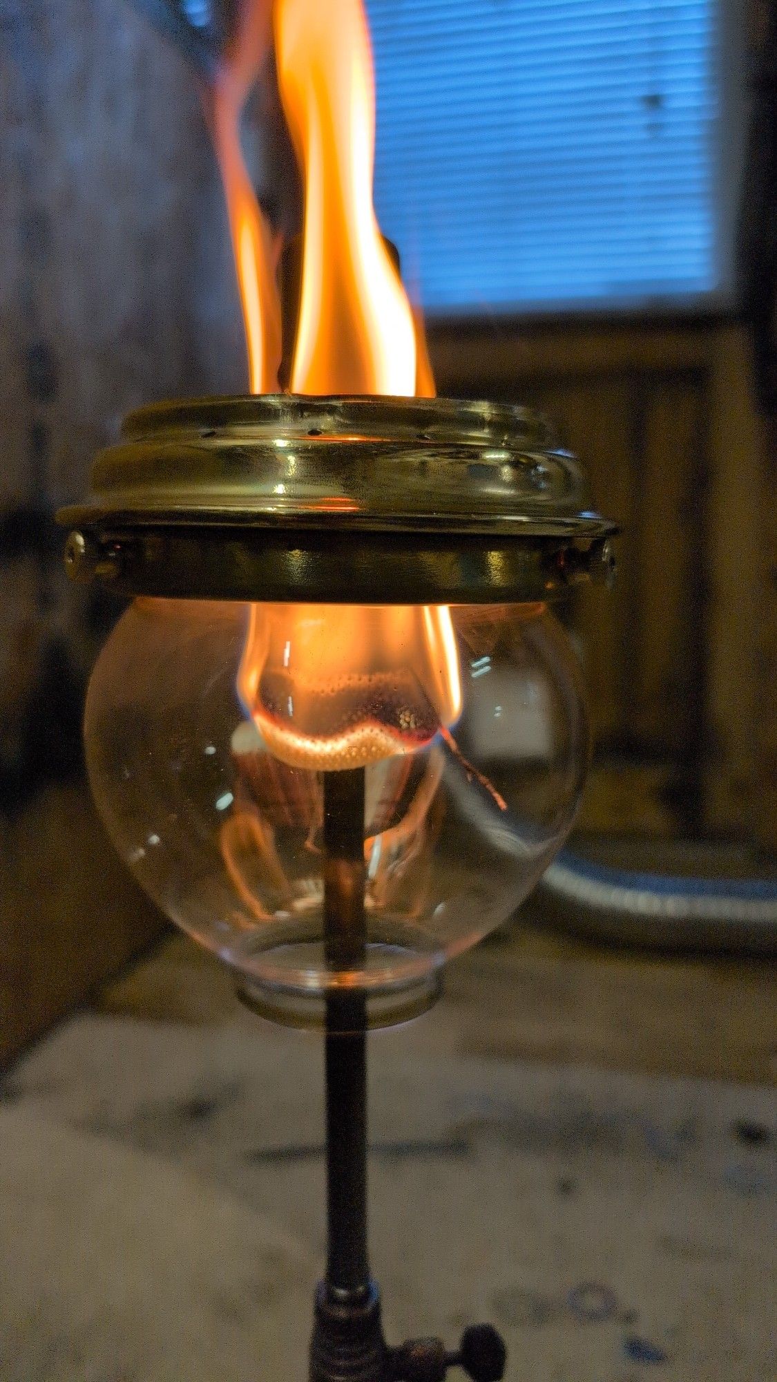 A close up of a Tilley table lamp, burning with an orange flame when it ought to be white