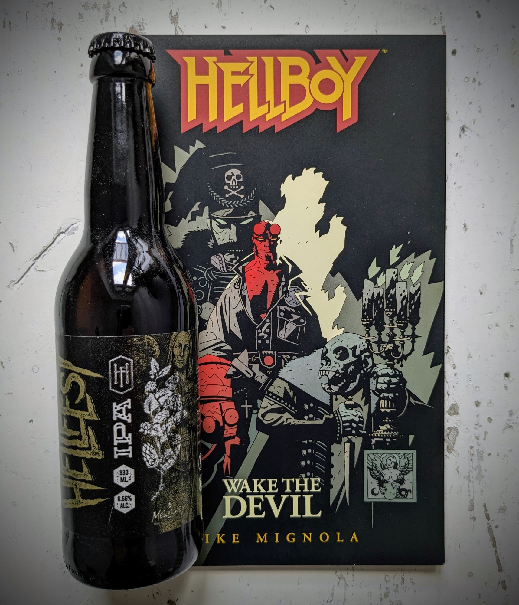 Eine Flasche „Hellfest IPA“ von der französischen Brauerei Mélusine liegt auf dem Comic „Hellboy: Wake the Devil“ von Mike Mignola (Darkhorse Comics). Sowohl auf der Flasche als auch auf dem Cover sinf allerlei unheimliche Gestalten in schwarz-grauen Tönen abgebildet. In der Mitte des Covers steht ein unbeeindruckt brennender Hellboy.