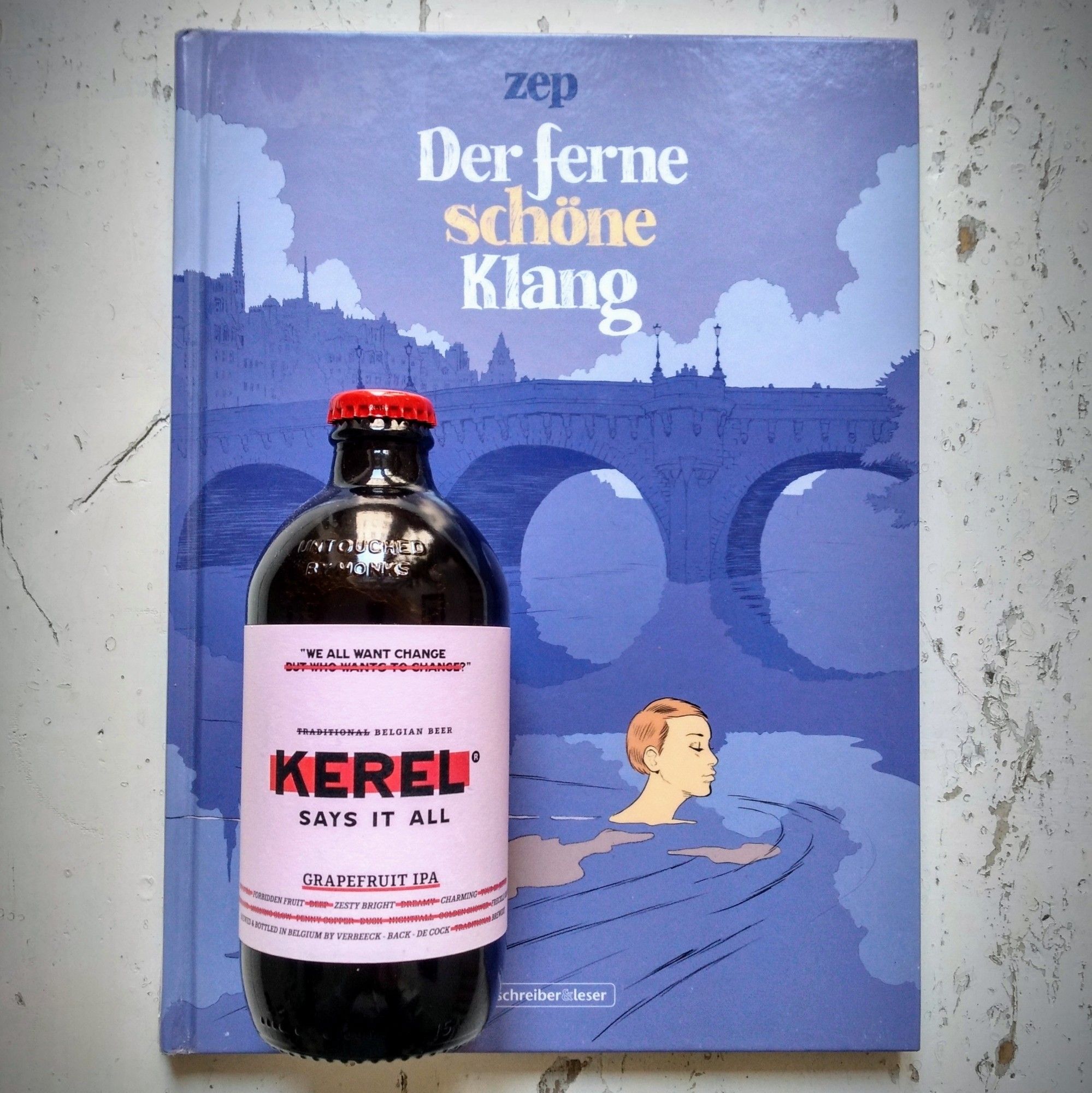 Flasche Grapefruit IPA von Kerel, darunter der Comic „Der ferne schöne Klang“ von Zep, erschienen bei Schreiber & Leser. Auf dem Comic ist eine Frau zu sehen, die entspannt vor einer Pariser Brücke durch die Seine schwimmt.