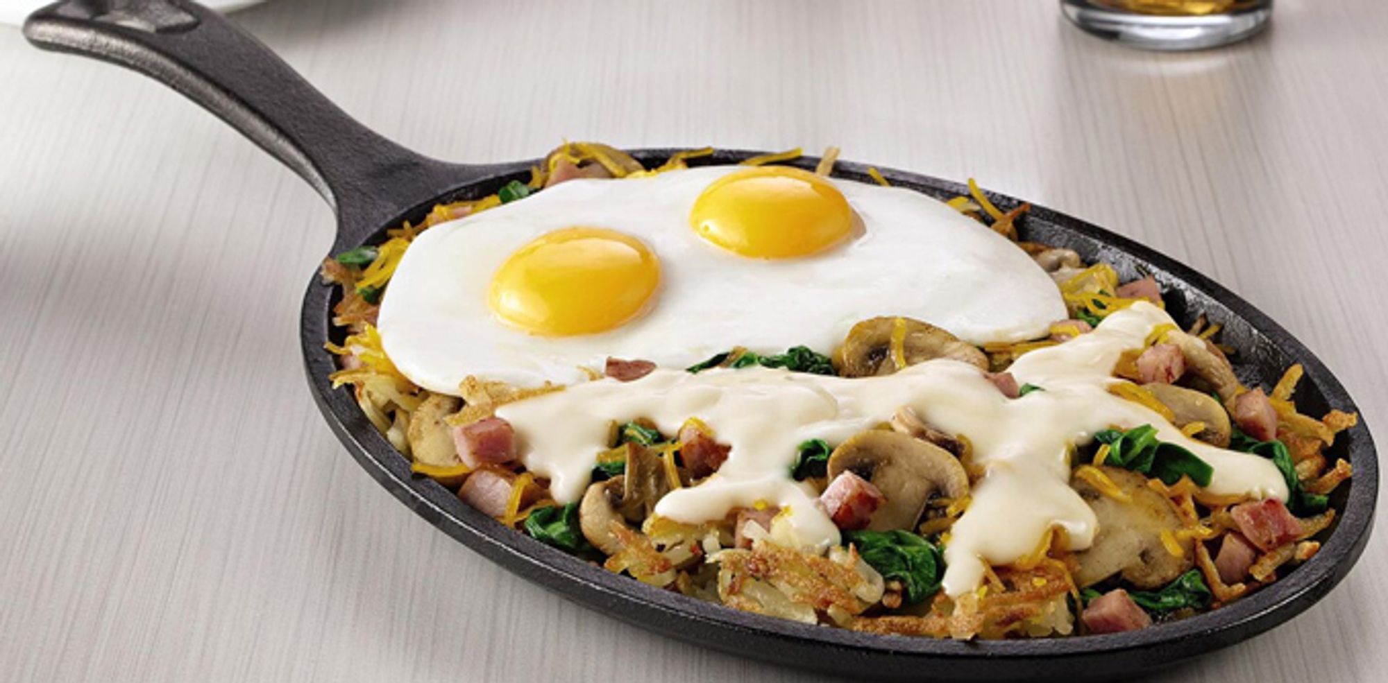 Two sunny side up eggs, on a bed of diced ham and shredded potatoes, with broccoli and mushrooms, in a skillet