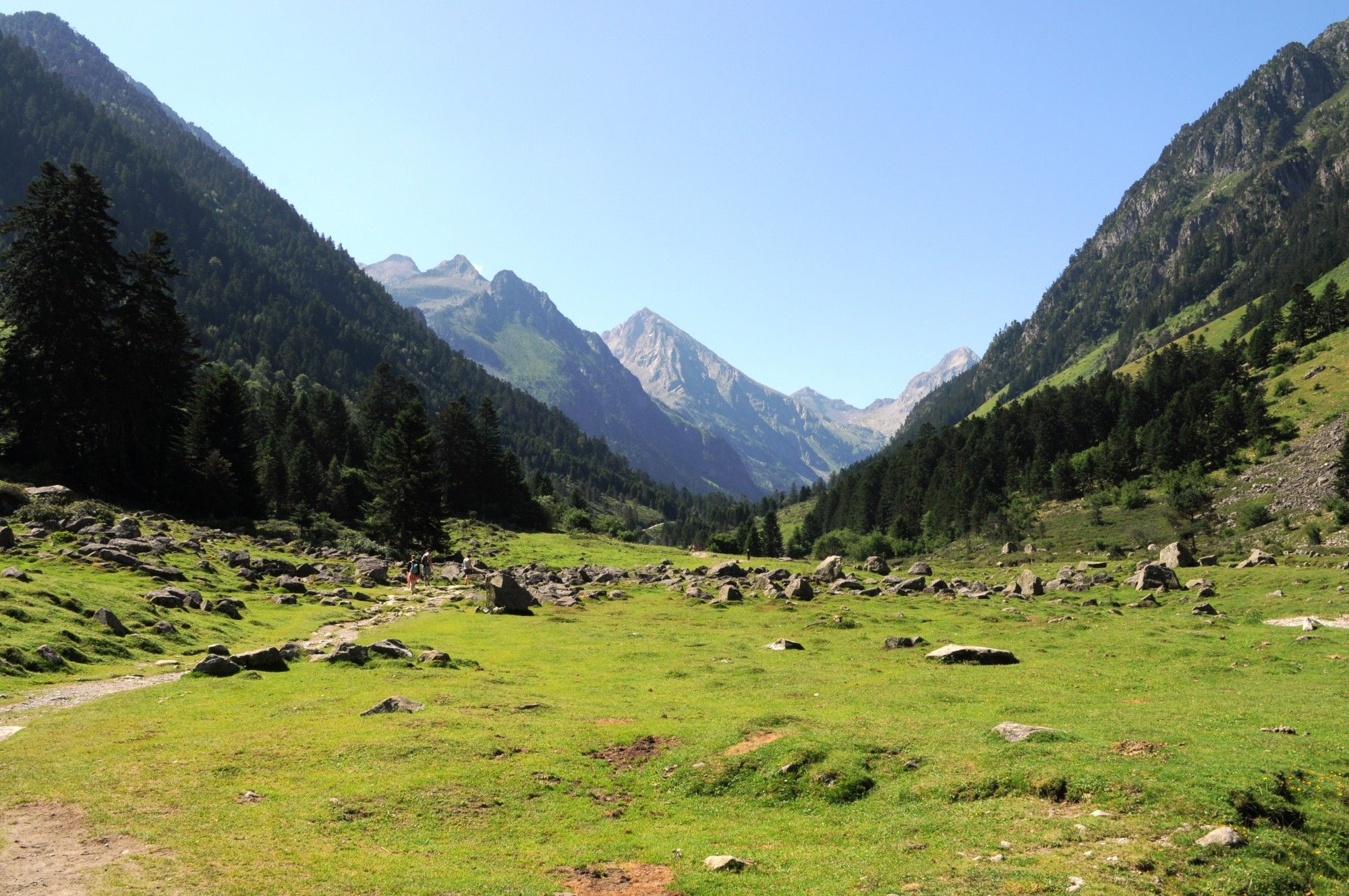 une vallée de montagne avec un chemin, un petit col qui se dessine là où se rejoignent deux flancs de montagnes au fond des sommets plus élevés