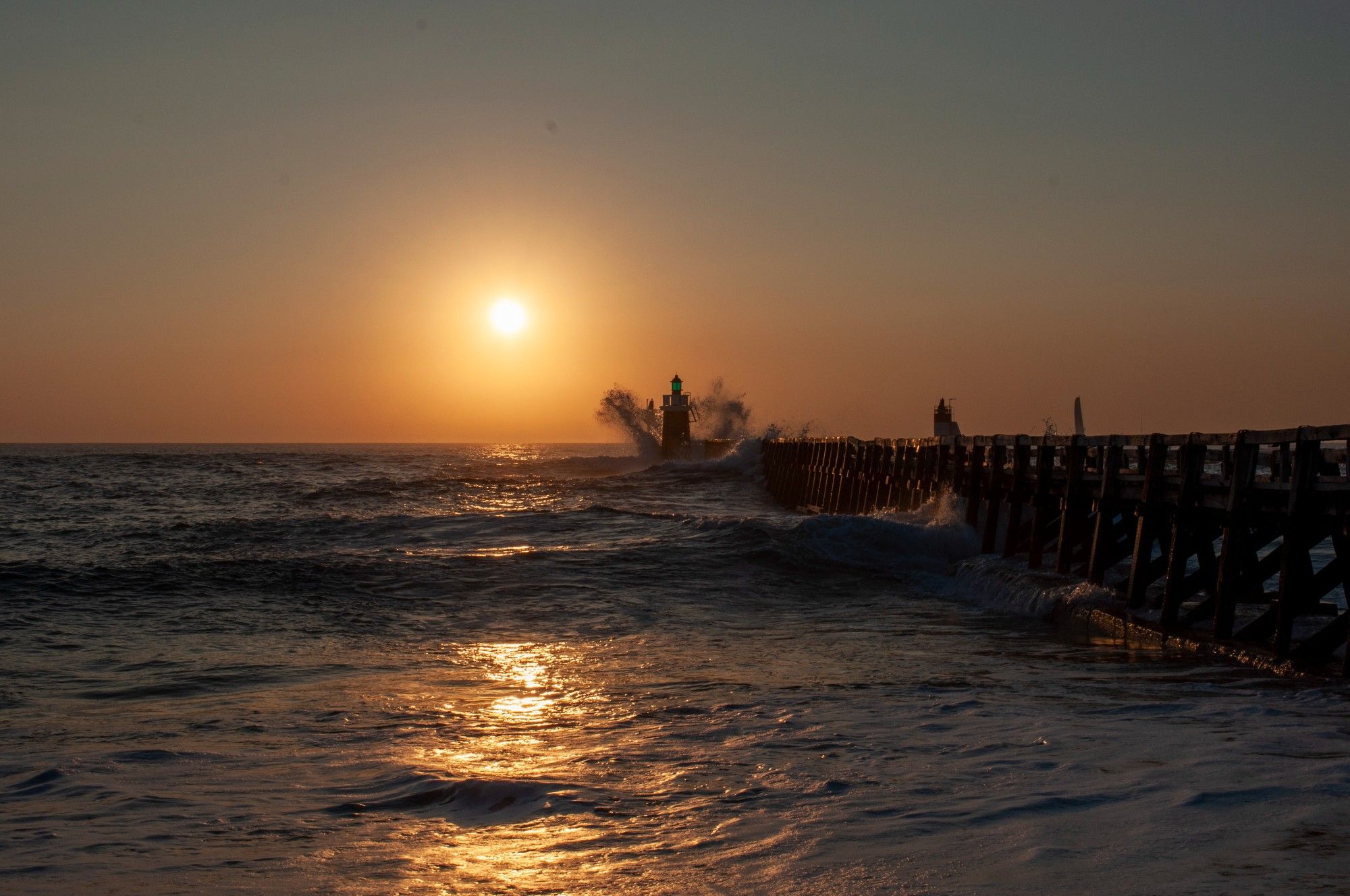 l'estacade de Capbreton au couché du soleil, la houle déferle sur le phare et projette des embruns