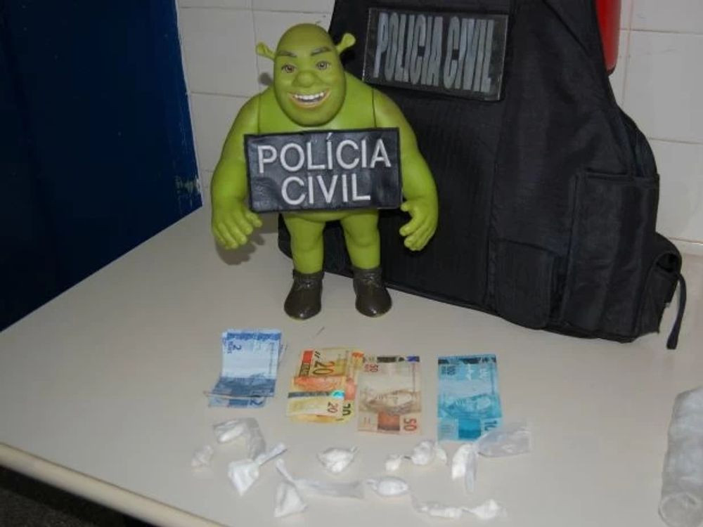 Shrek figurine with a Policia Civil sign in hand on a table with some drugs and money. DrugBust