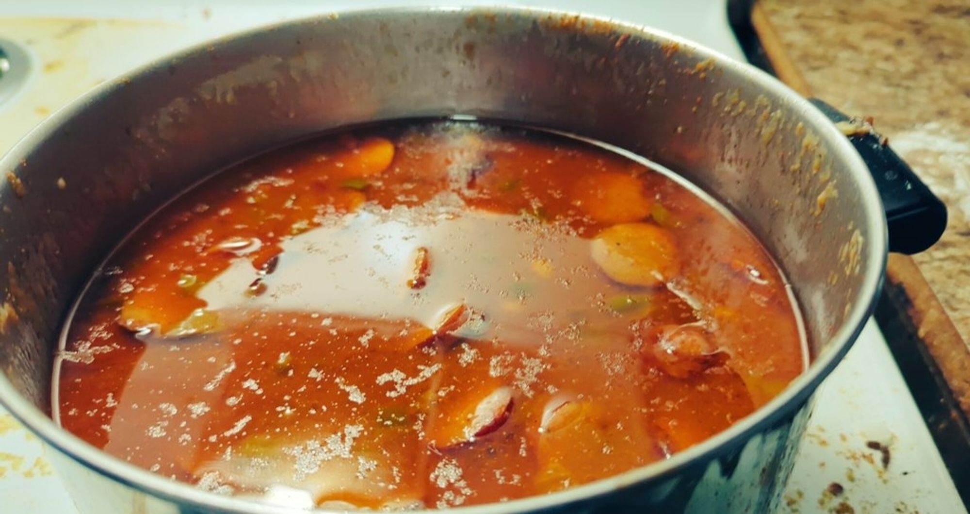 A pot on a stove filled with various meats and vegetables, submerged in liquid.