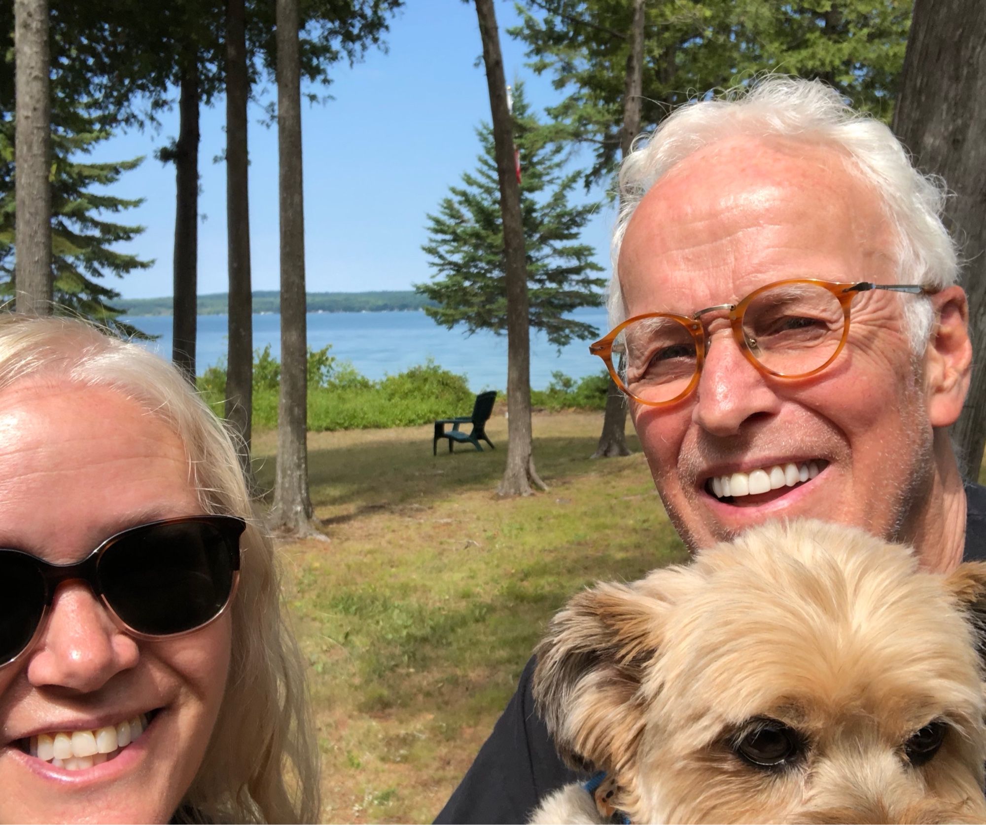 A white woman in her 50s (me!) next to a white man in his 80s (Dad!) smiling with a dog in a beautiful Michigan setting